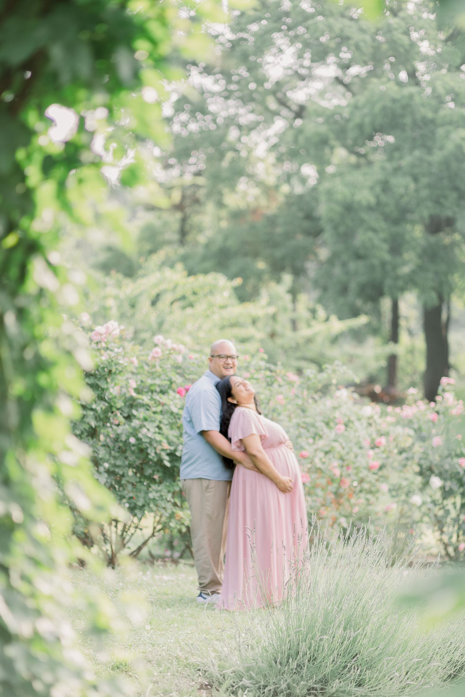 A couple shares a tender moment among blooming rose bushes and lavender in a romantic garden setting.