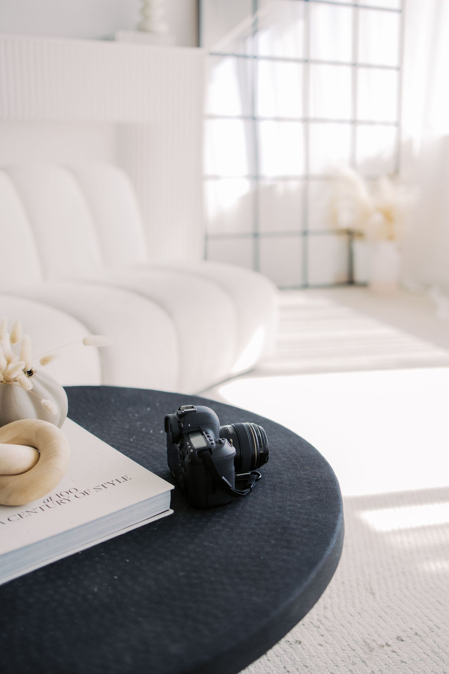 Black camera lens on dark textured surface with white pages and natural window light in bright minimalist setting.