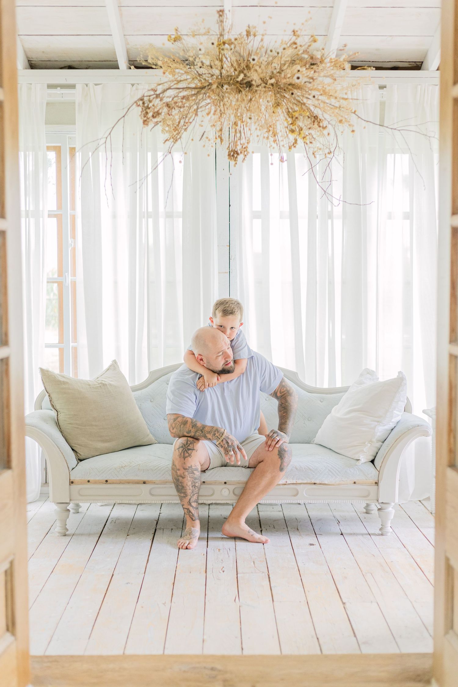 Two people sit on a bright white floor in a minimalist room with natural light streaming through sheer curtains.