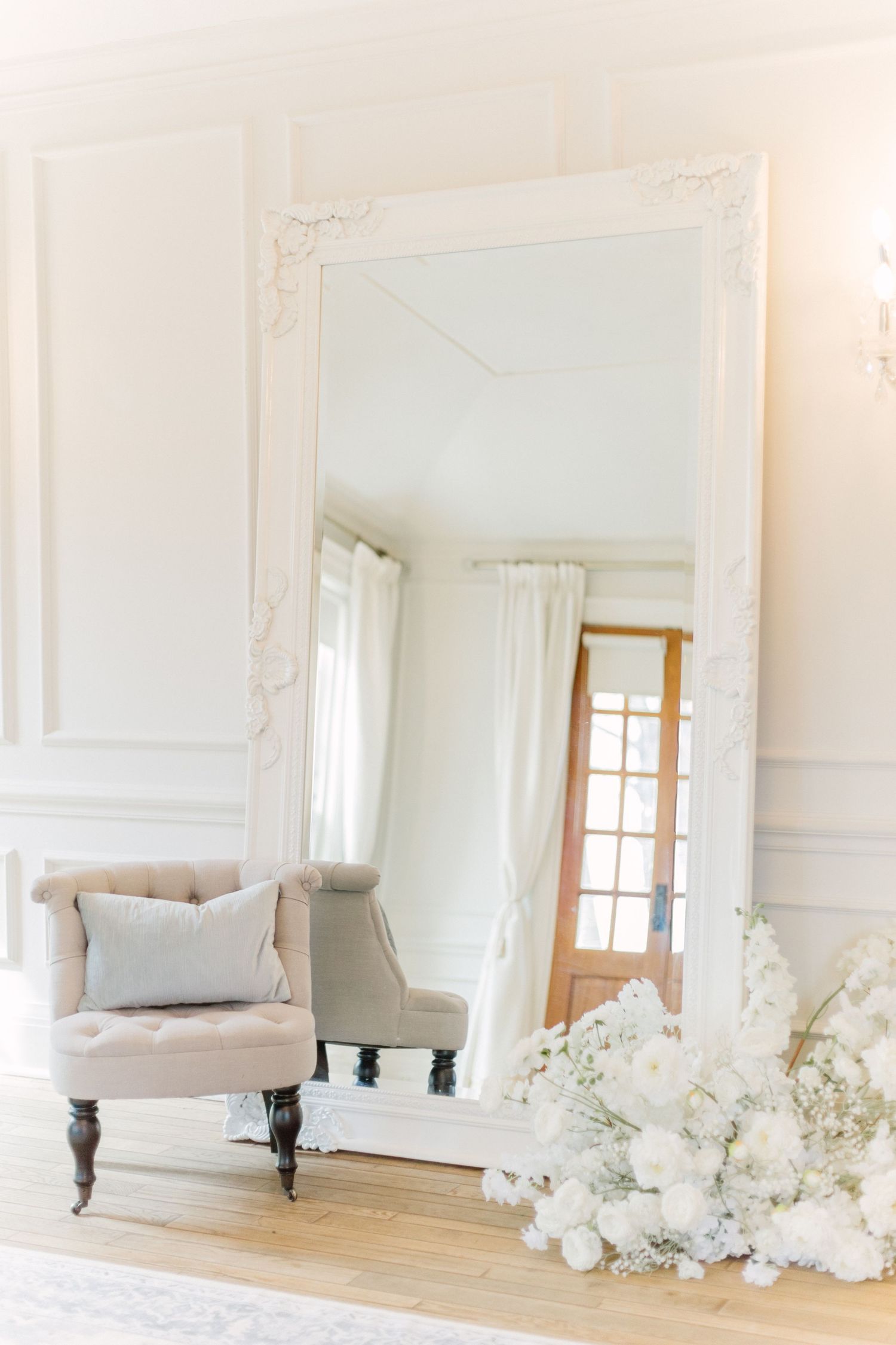Elegant white studio space with ornate moldings, hardwood floors, and white floral arrangements by the wall.