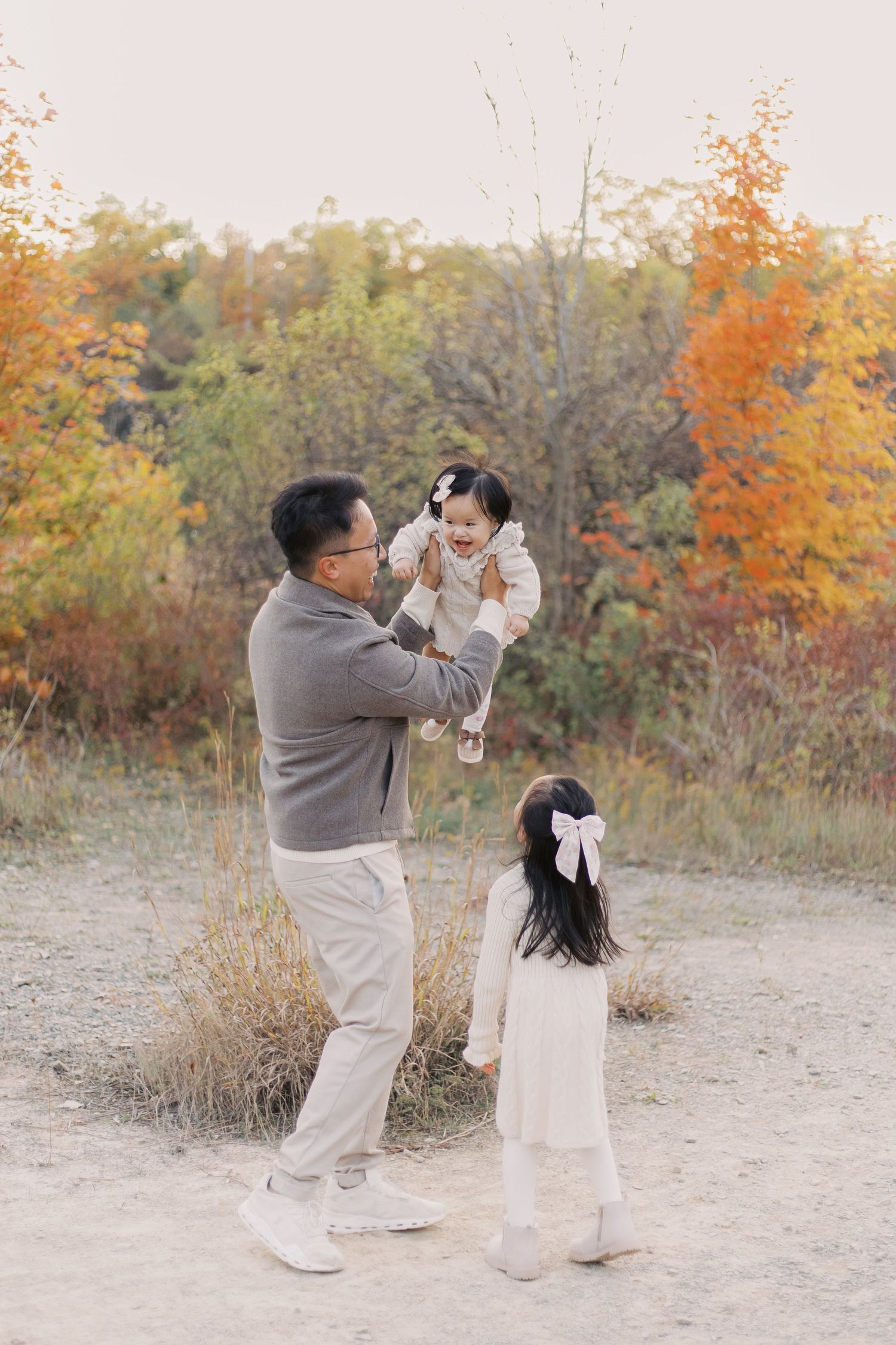 A family enjoys playful moments together on a path surrounded by vibrant fall colors and autumn trees.