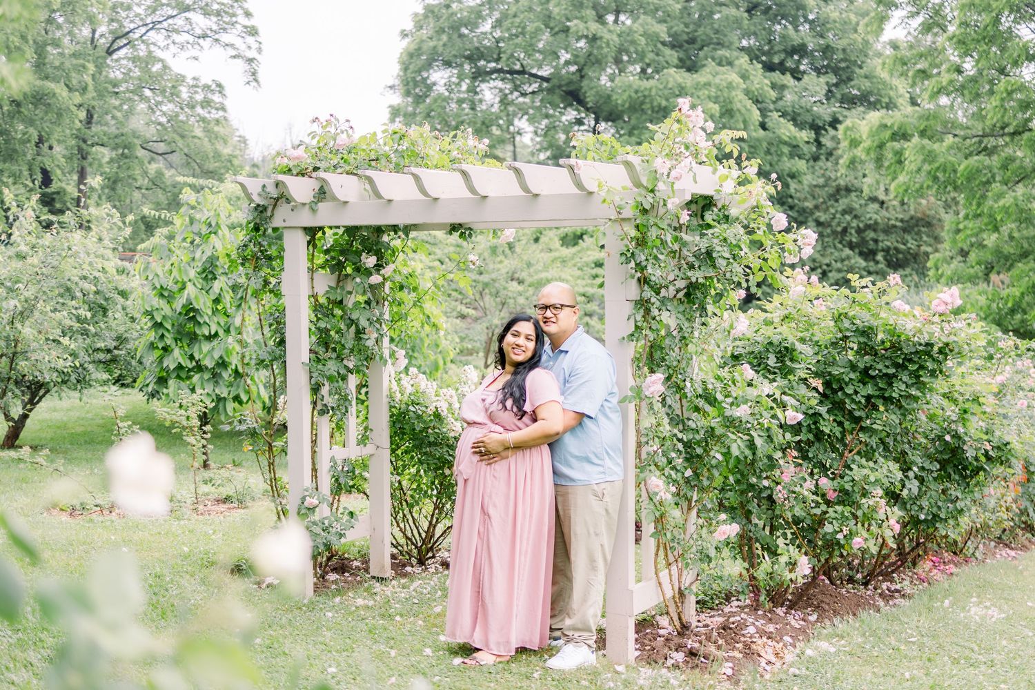 A couple shares a tender moment in a lush garden setting surrounded by blooming flowers and greenery.