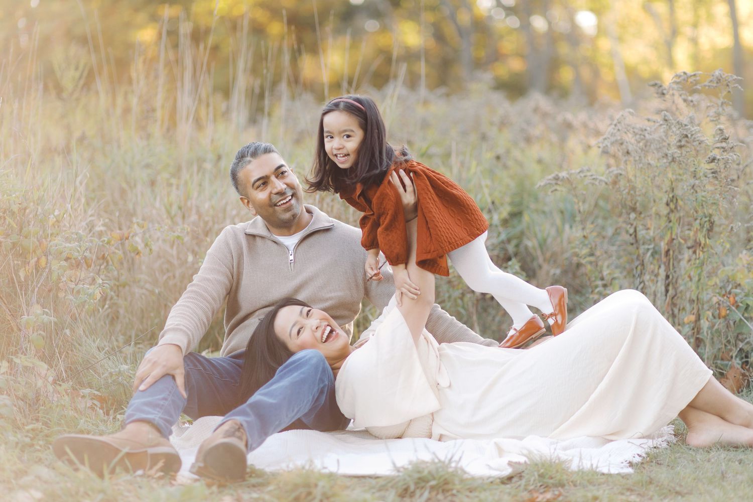 Family enjoying a tender moment together in a sun-drenched autumn field with golden grass and warm lighting.