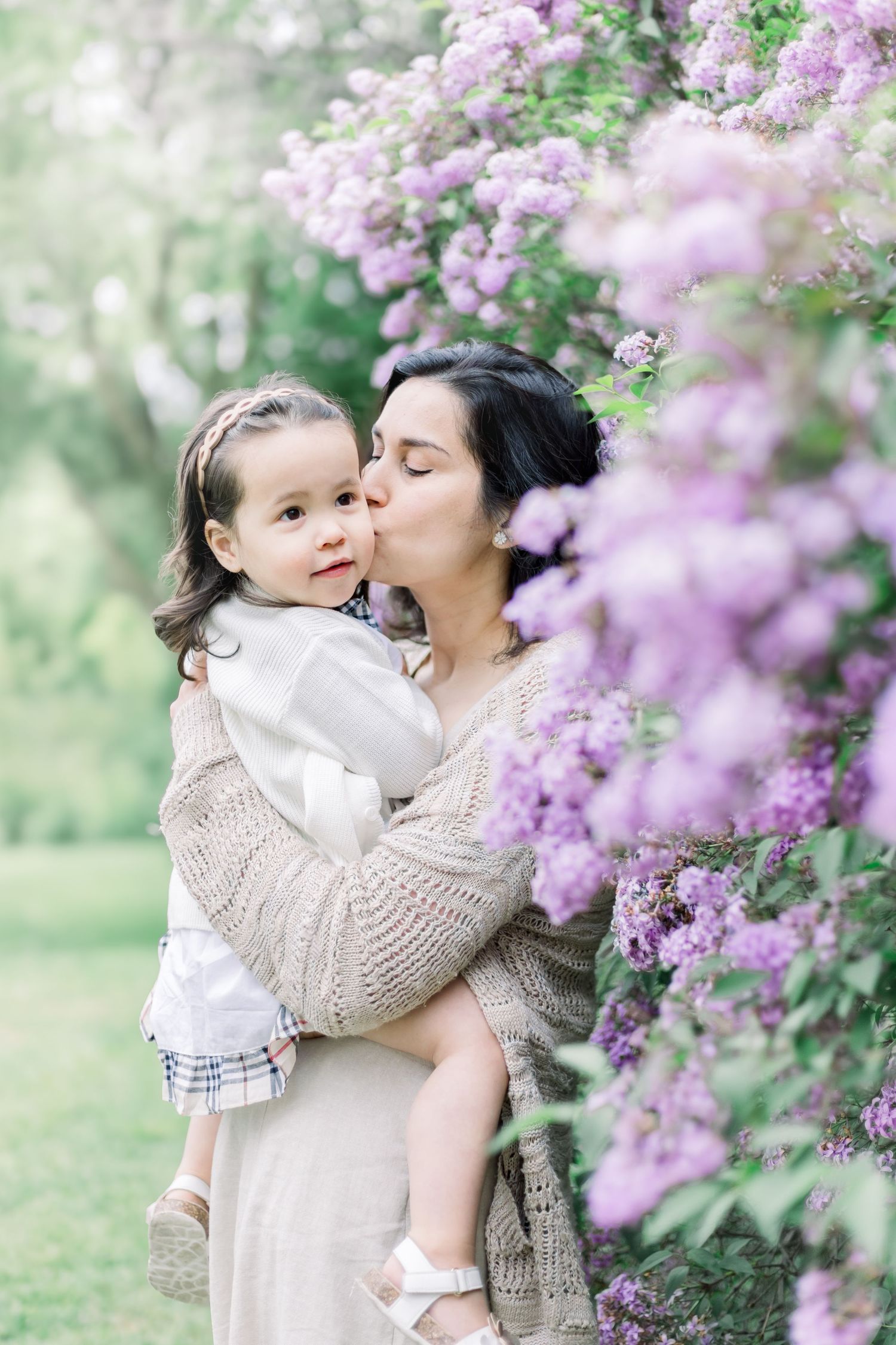 Mother and child share tender moments among blooming pink lilac bushes in a spring garden setting.