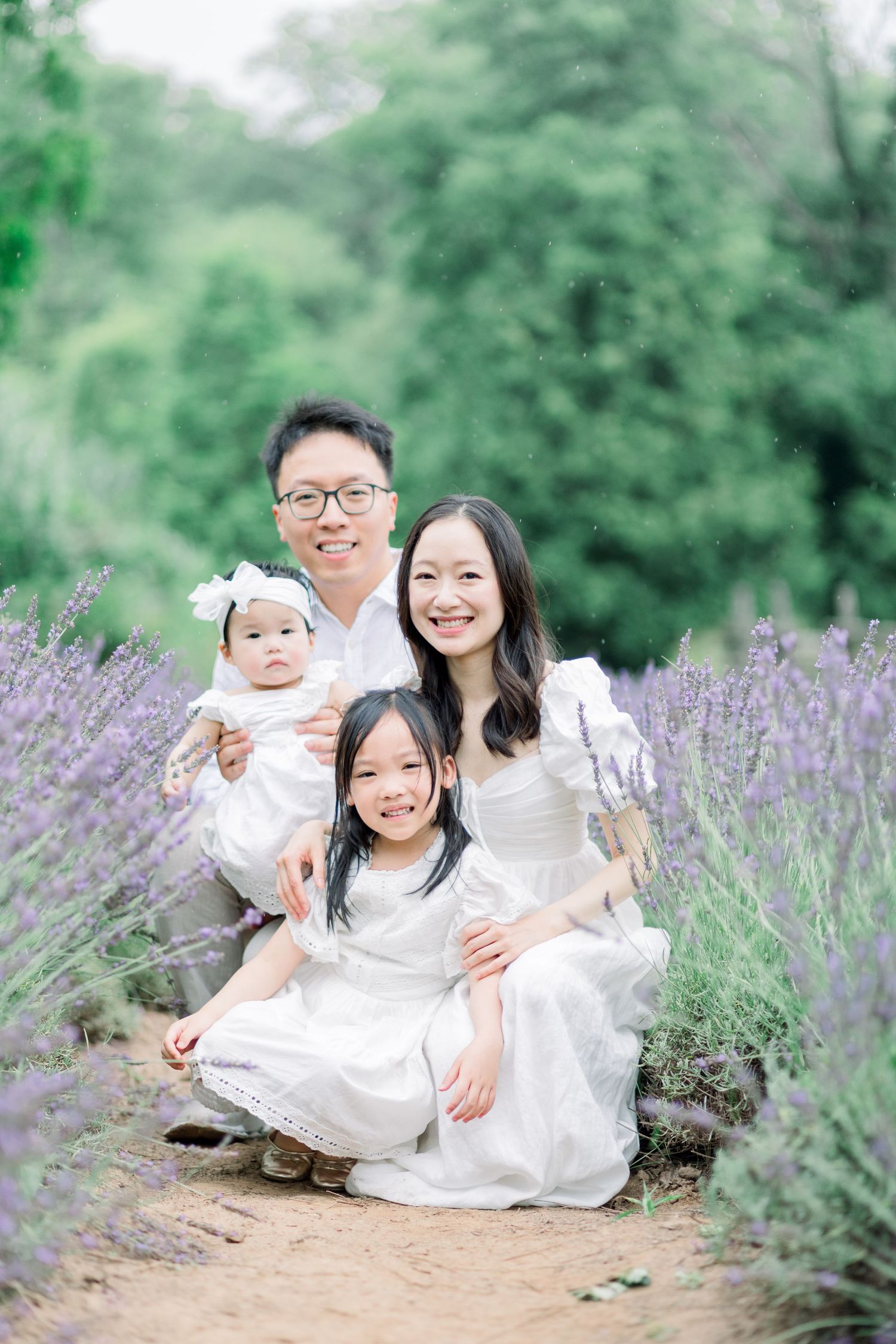 A family portrait session in a blooming lavender field with soft natural lighting and everyone wearing white outfits.