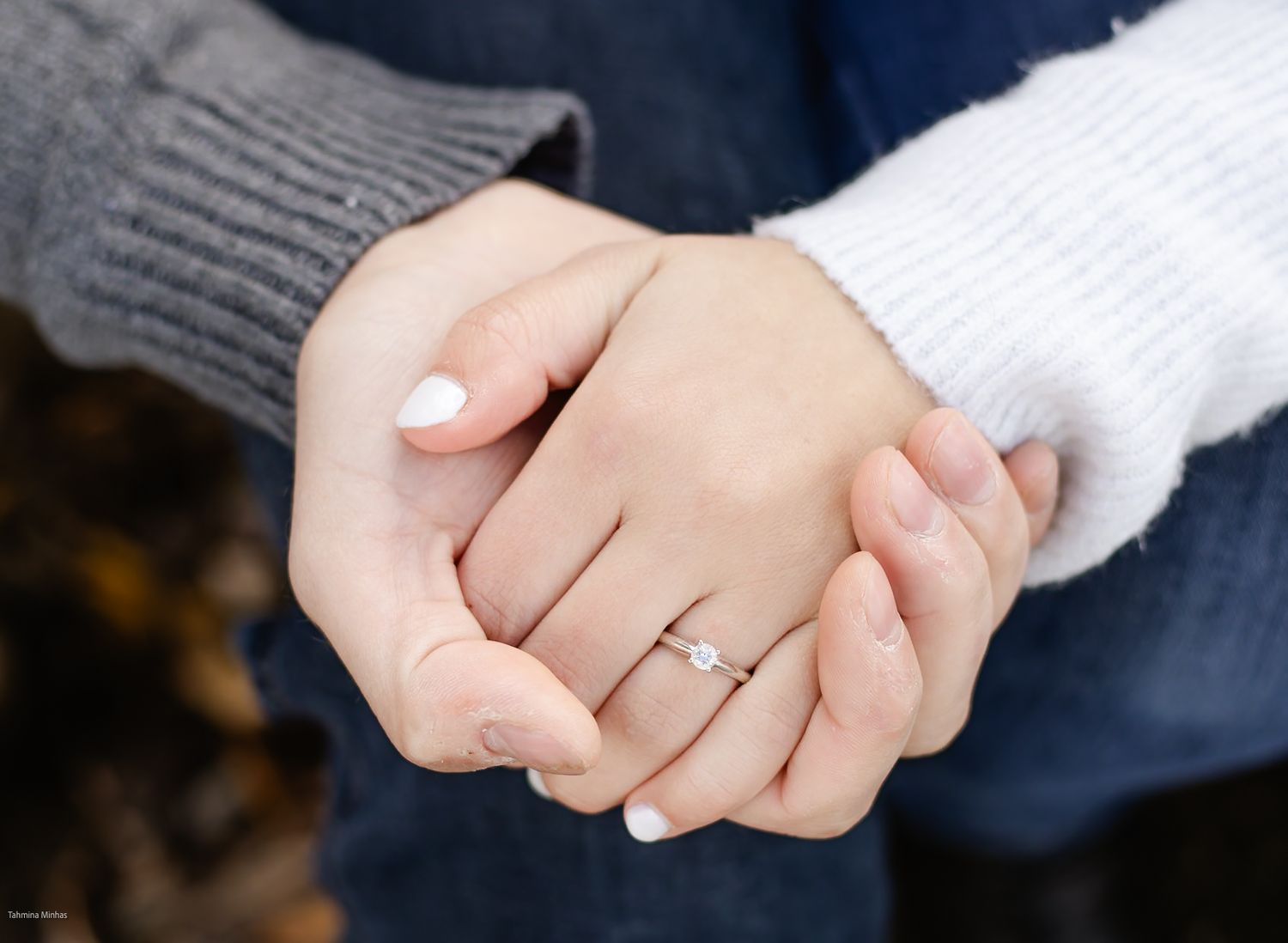 Close-up view of two hands clasped together, with a diamond engagement ring visible on one hand.