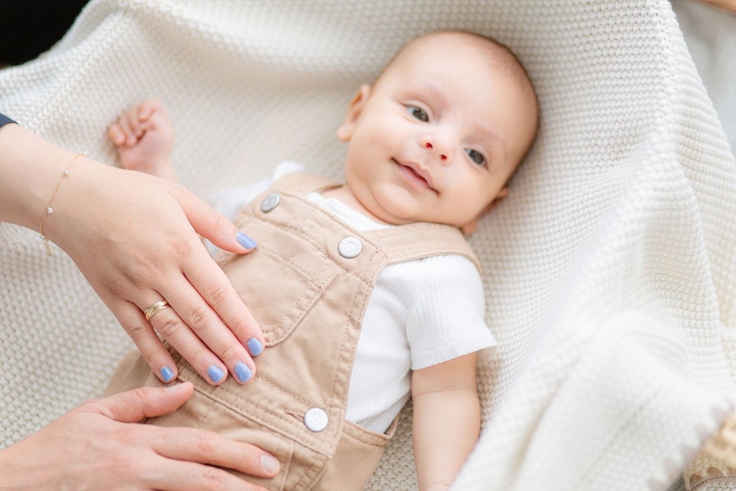 Gentle hands massage a baby's belly while lying on a soft white knitted blanket.