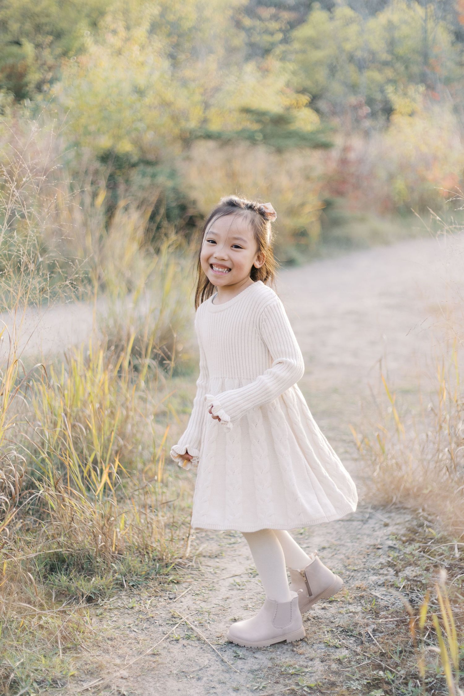 A series of candid photos showing a young child in a cream-colored dress twirling and playing outdoors in autumn scenery.