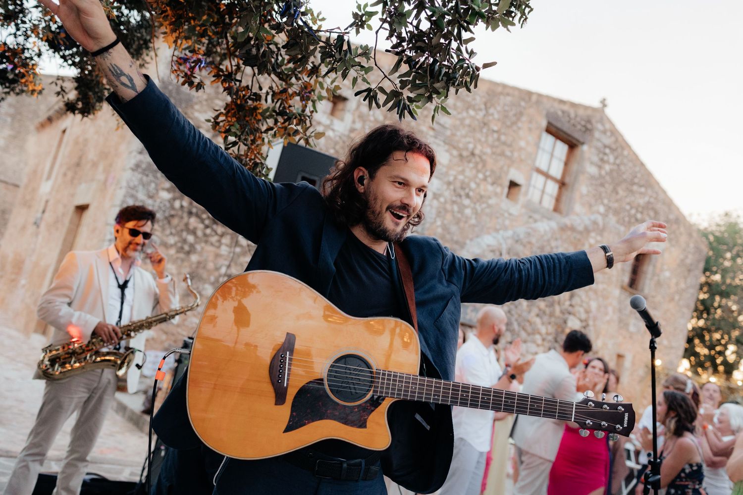 Musician performs with acoustic guitar at outdoor celebration while crowd cheers.