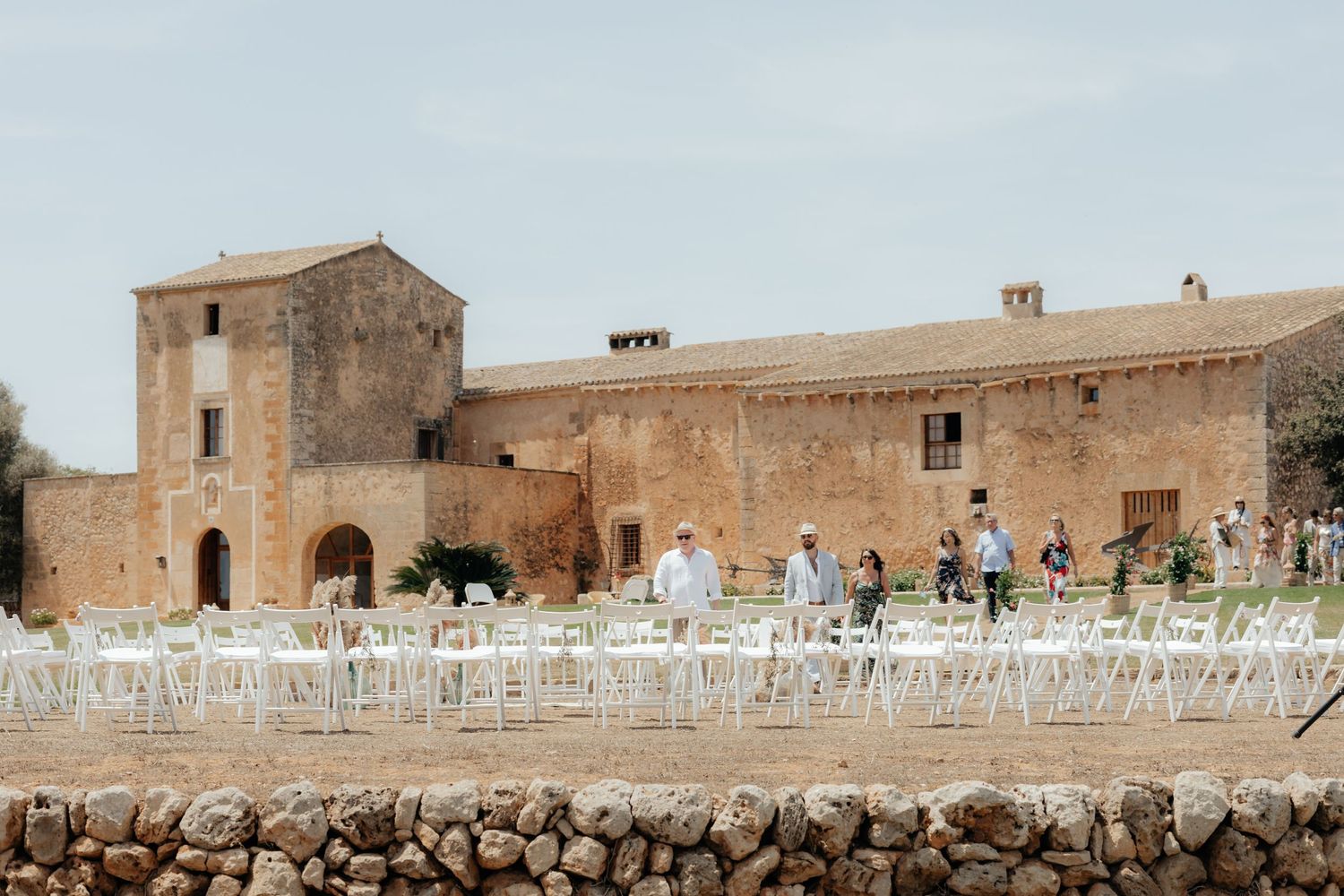 Rustic stone wedding venue with white chairs set up outdoors at historic Mediterranean estate building.