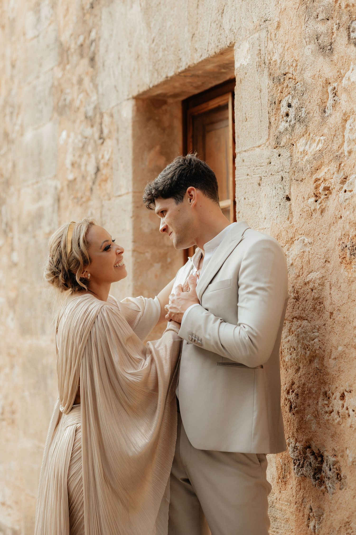 Romantic moment between couple against textured stone wall in warm sunlight.