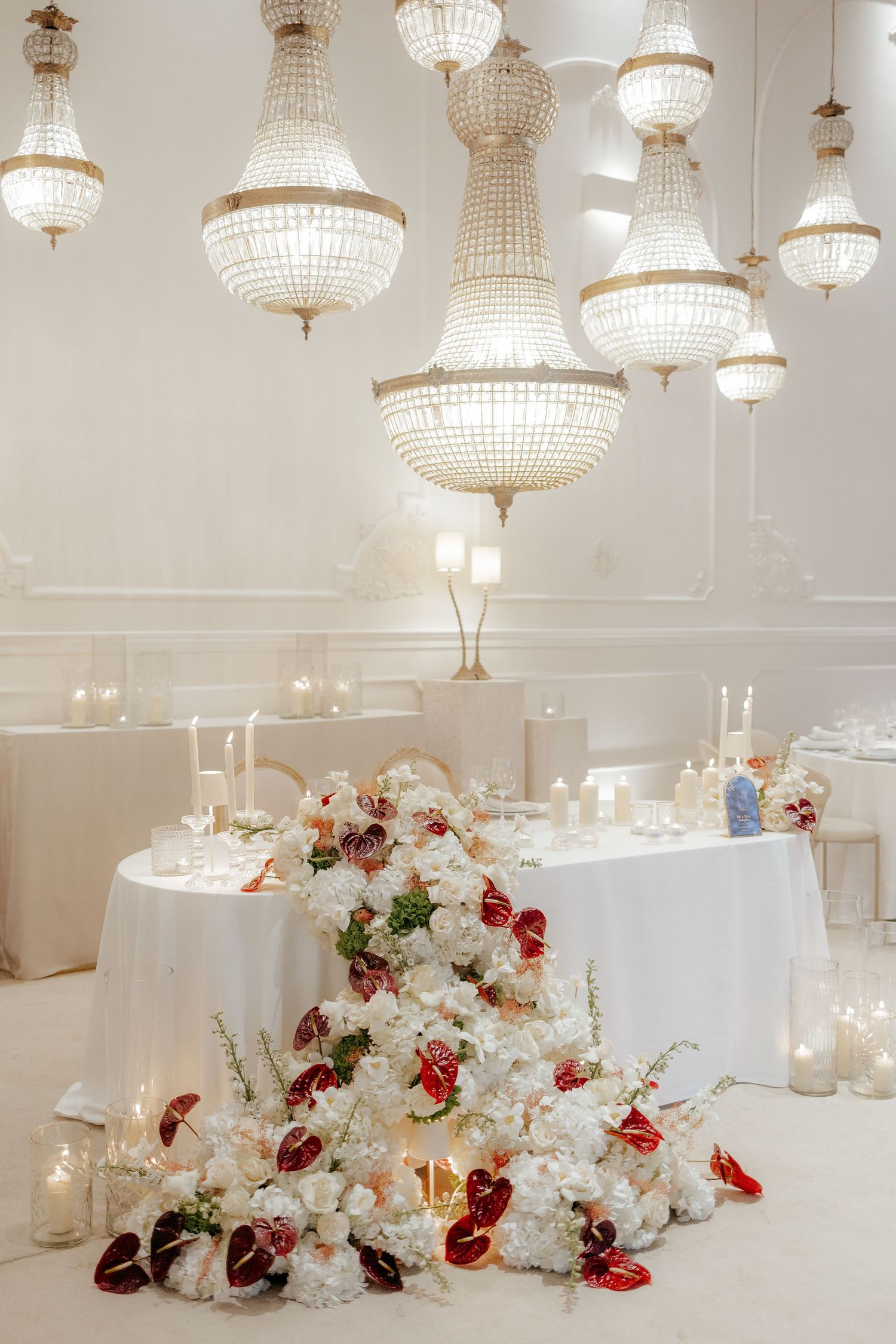 Elegant wedding table with red and white florals, candles, and chandeliers. Luxury decor in Portugal.