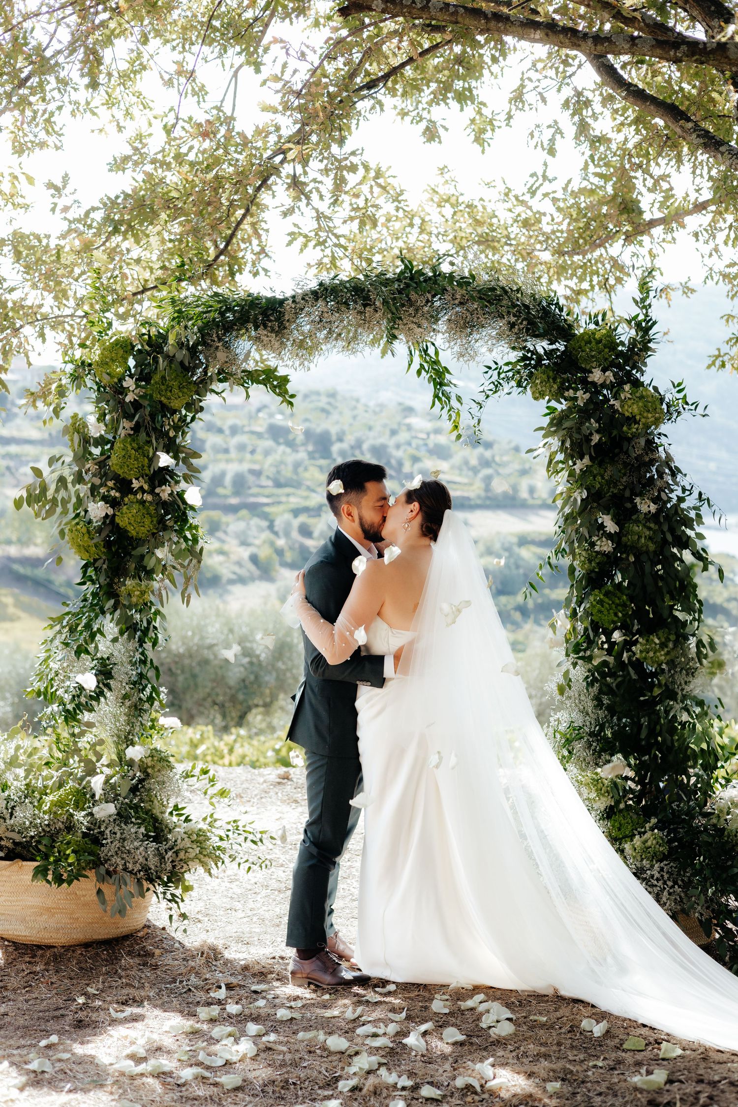 A romantic wedding ceremony under a lush greenery arch with mountain views in the background.