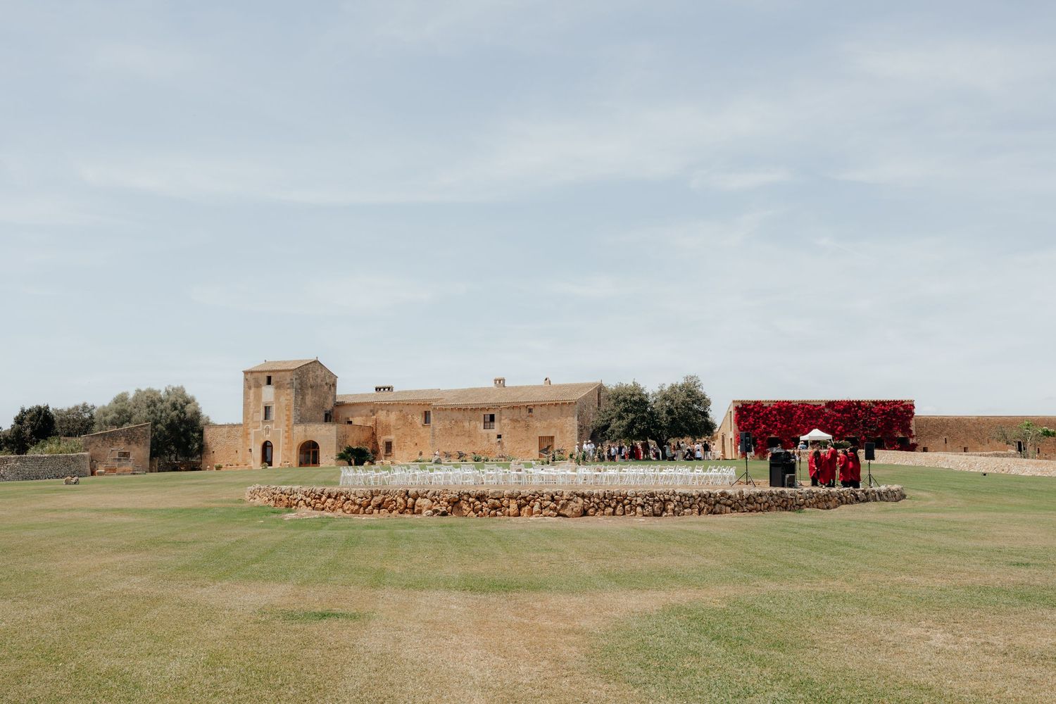 Mediterranean-style event venue with sandy stone buildings and a bold red floral installation under blue skies.