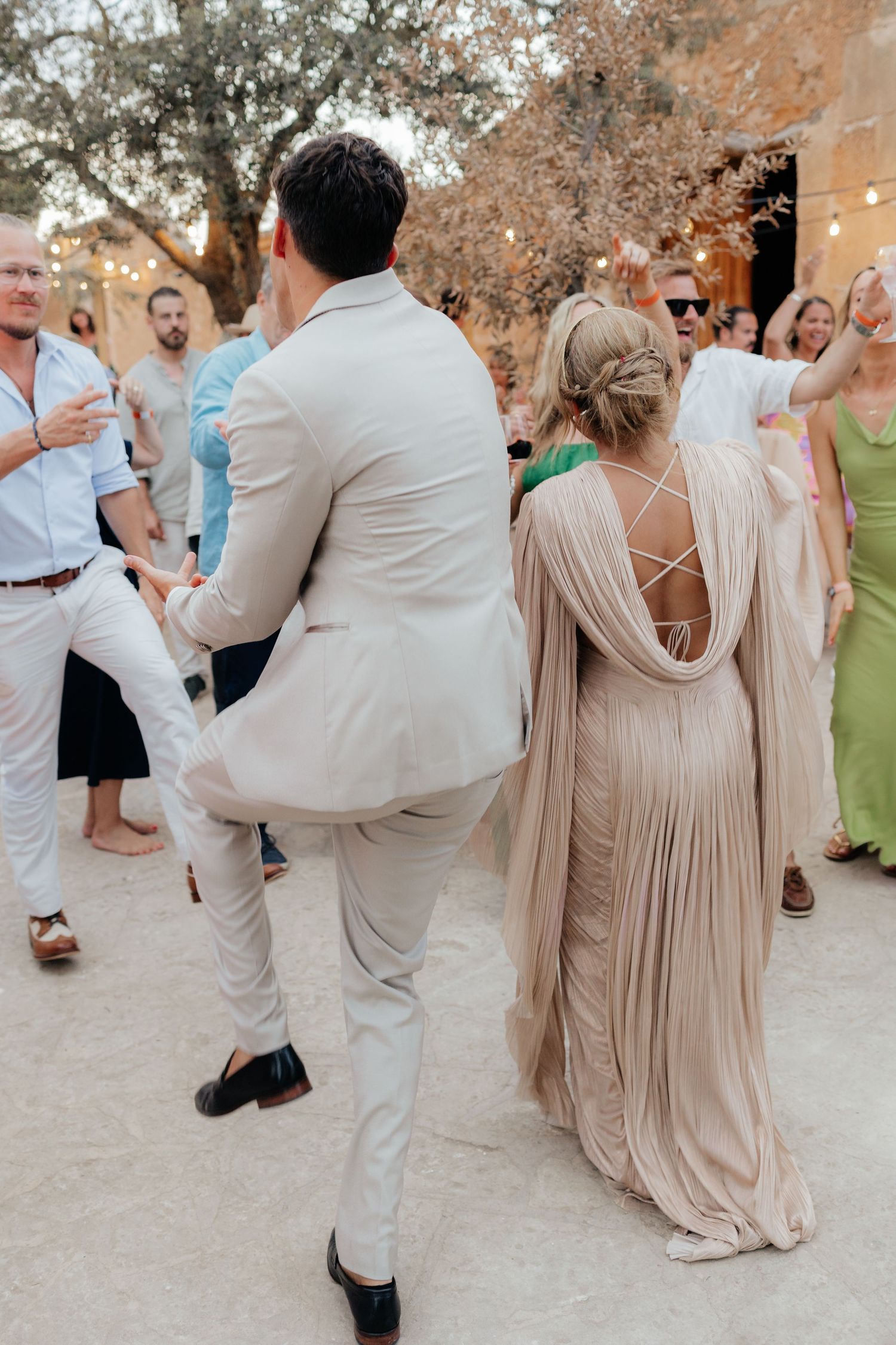Wedding party dancing outdoors with guests wearing light summer attire.
