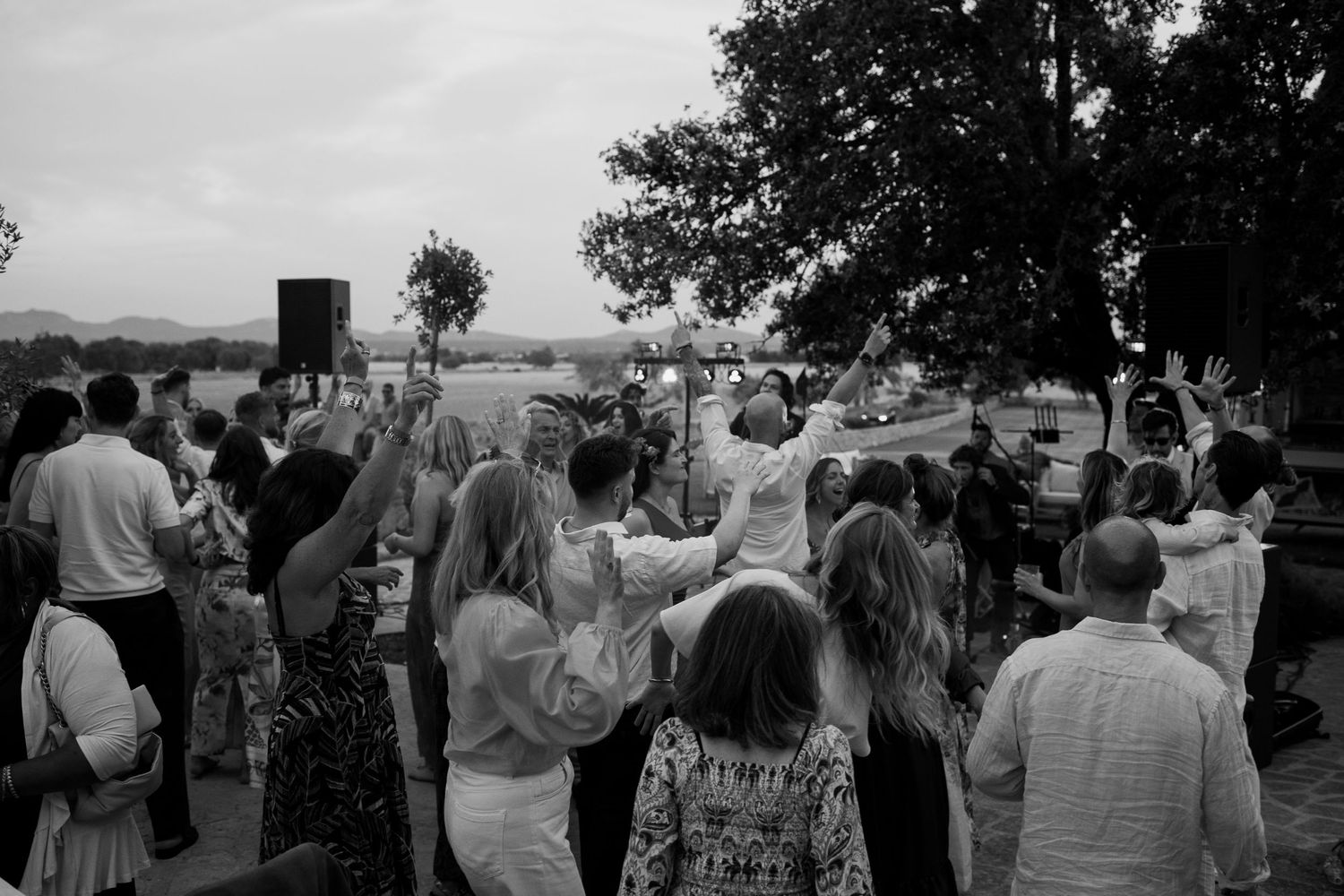 Crowd of guests celebrating at an outdoor event with raised hands in black and white photography.