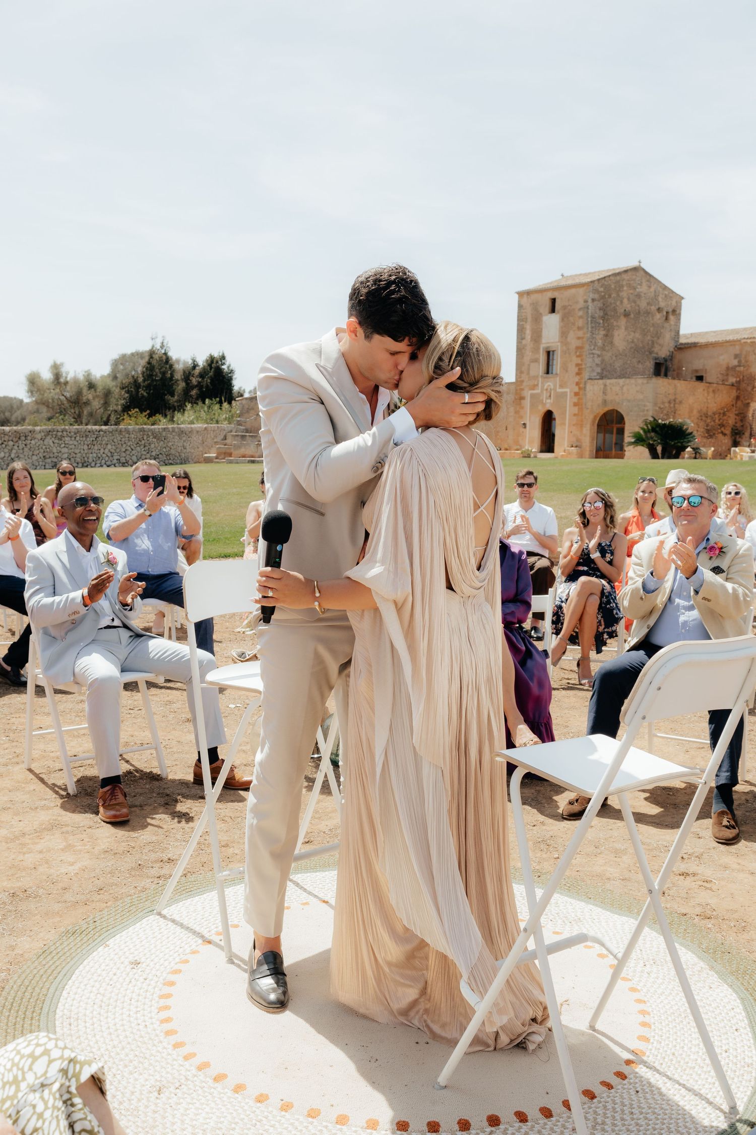 Wedding ceremony moment on a decorated circular platform with guests seated on white chairs.