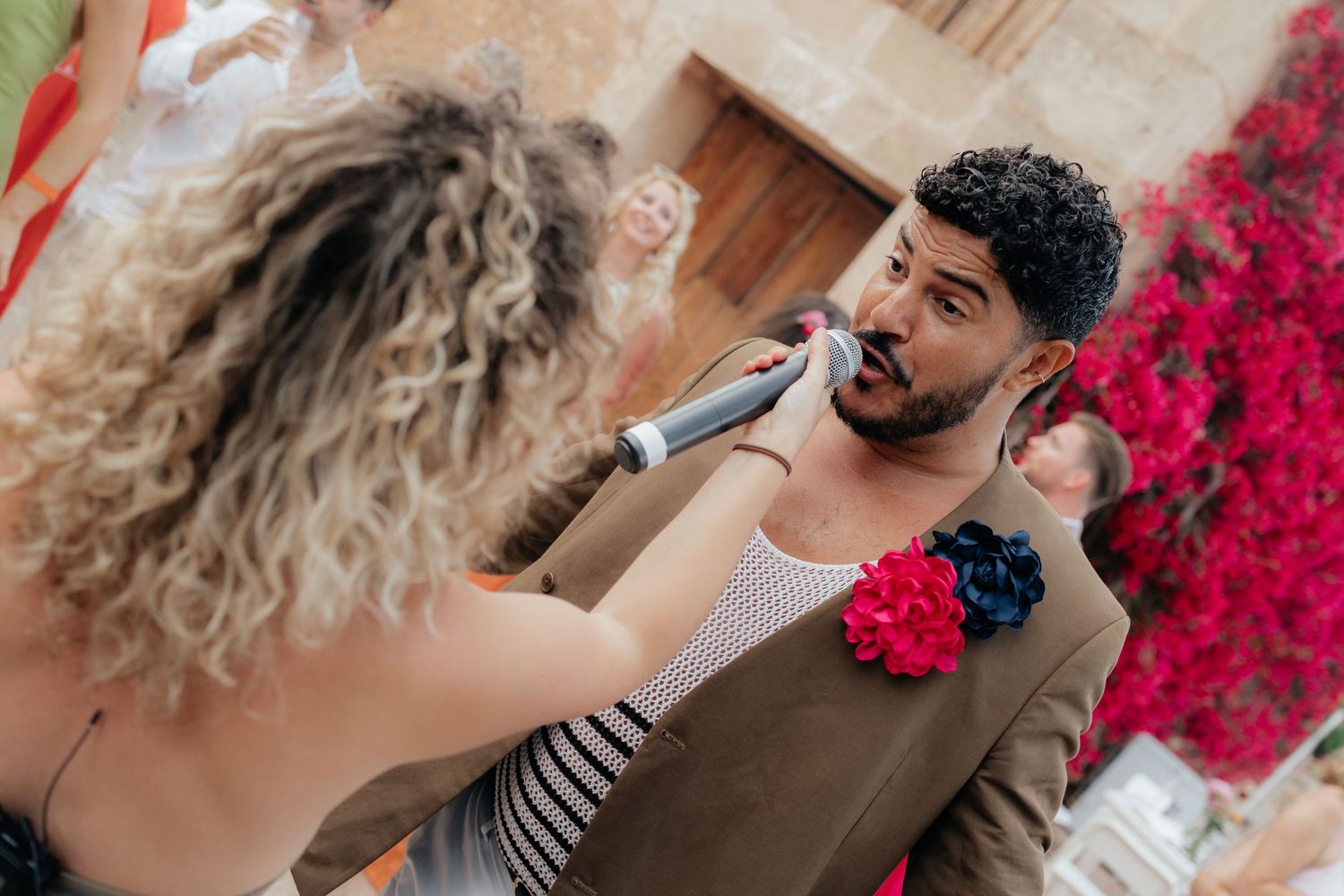 Professional applying makeup with brush to guest at outdoor event near vibrant pink floral decorations.