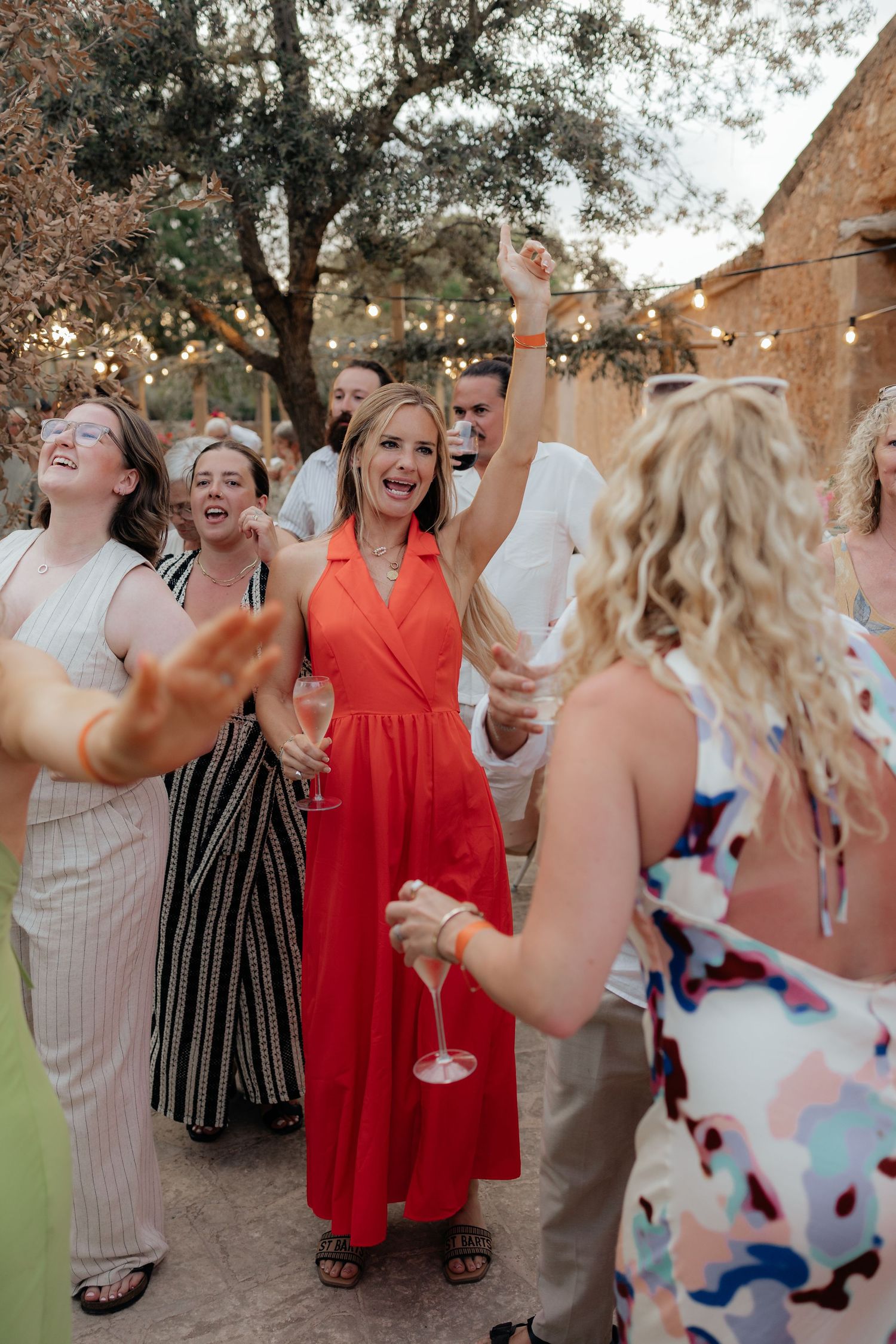Wedding guests dancing and celebrating at an outdoor reception with string lights.