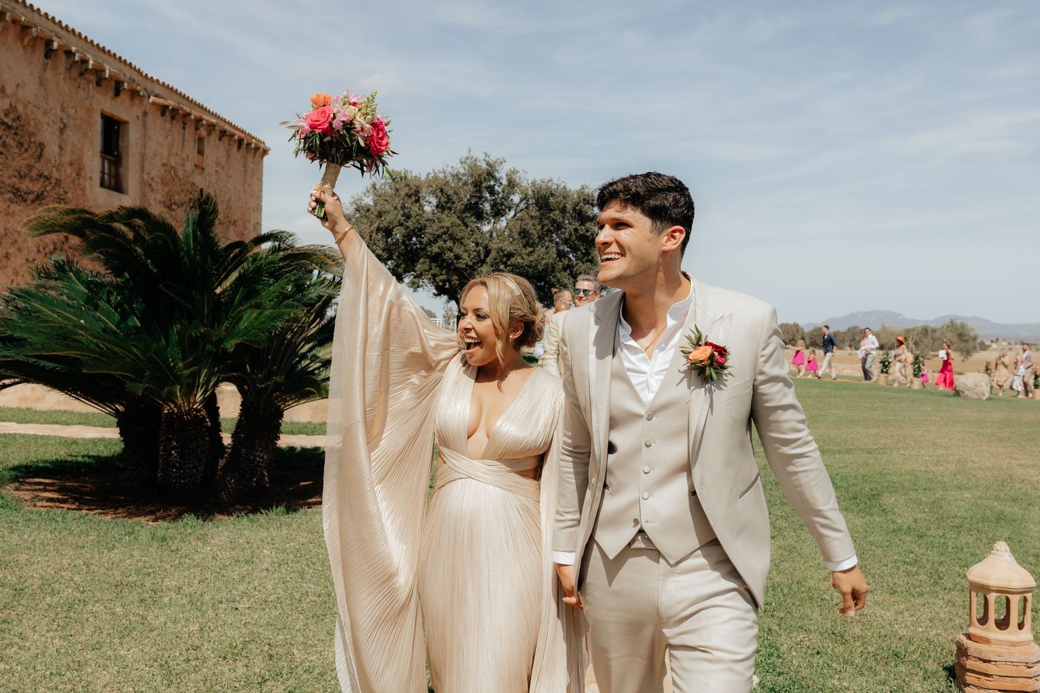 Newlyweds celebrating with raised bouquet against historic stone building backdrop.