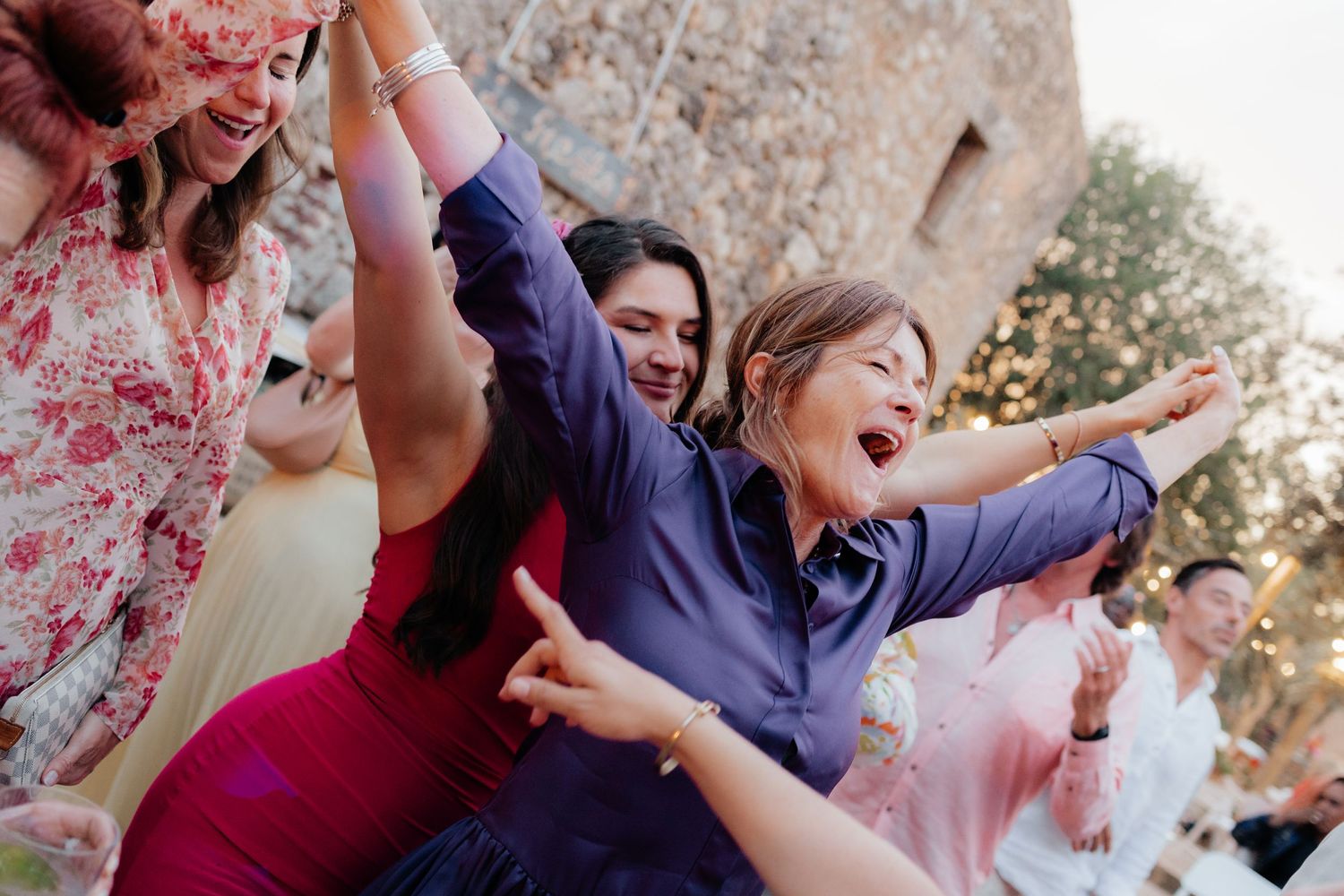 Wedding guests celebrating with arms raised in joyful celebration at outdoor reception.