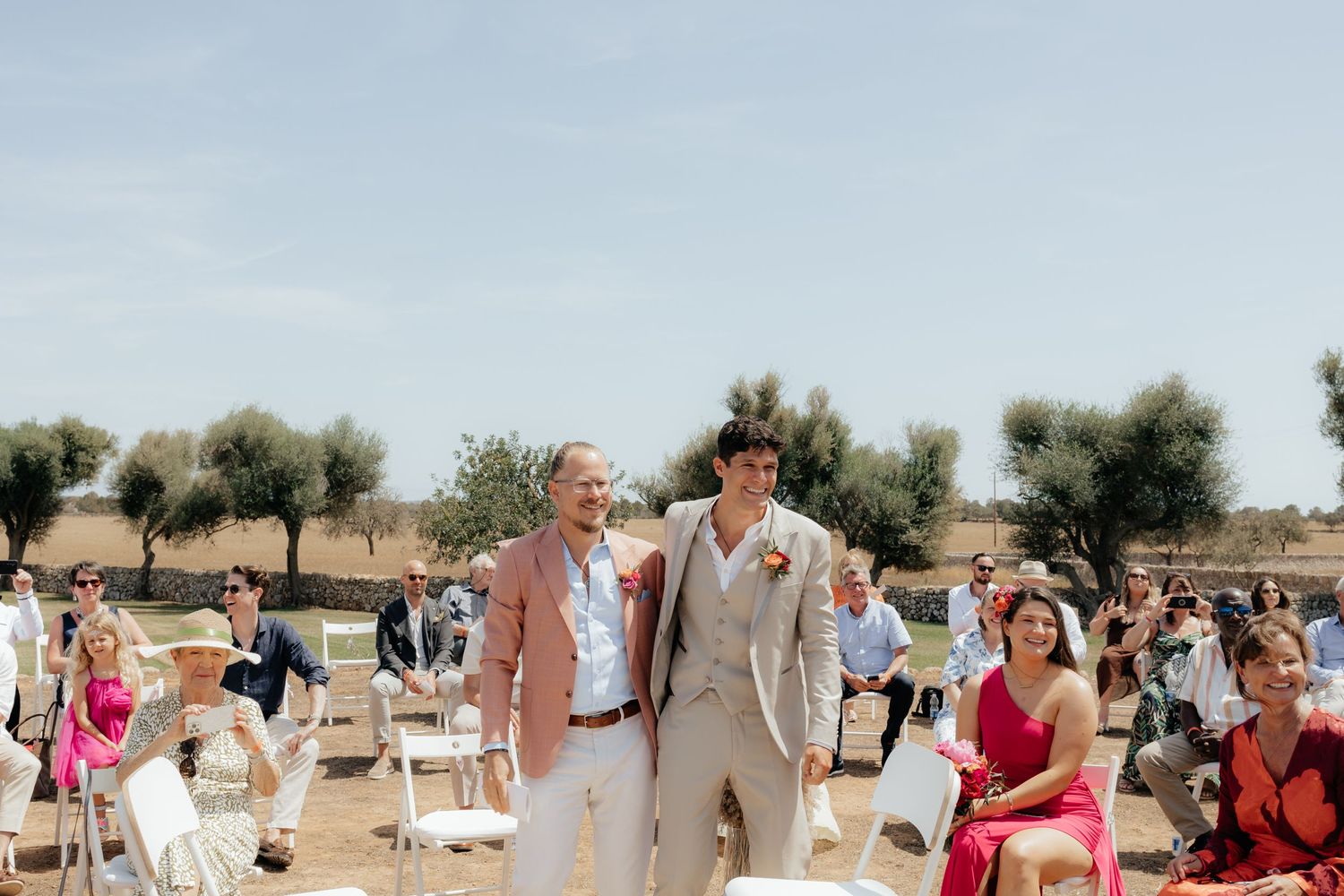 Happy wedding ceremony outdoors with people seated in white chairs at a sunny Mediterranean destination.