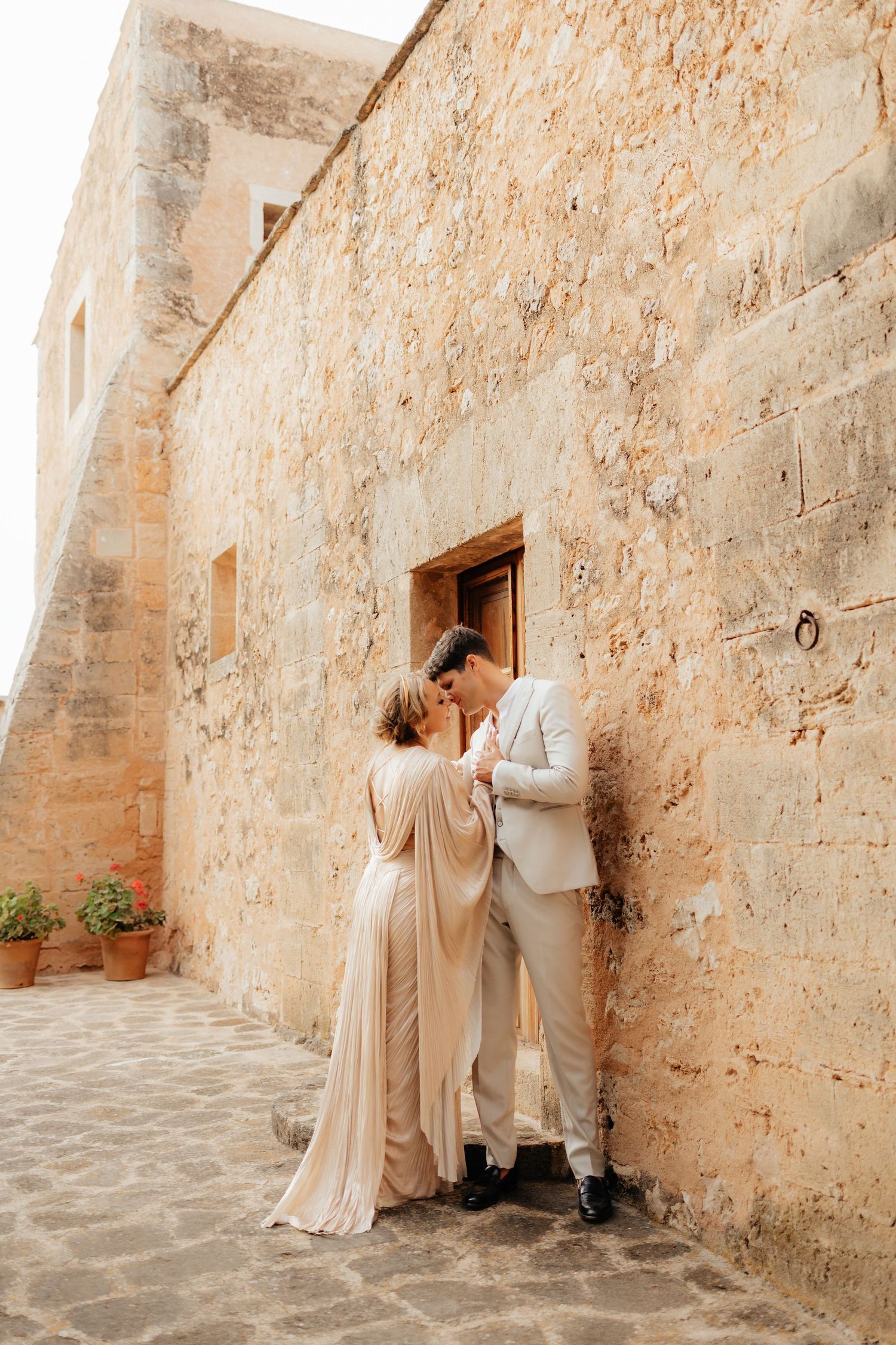 Romantic moment between a couple against a weathered stone wall at a historic Mediterranean venue.