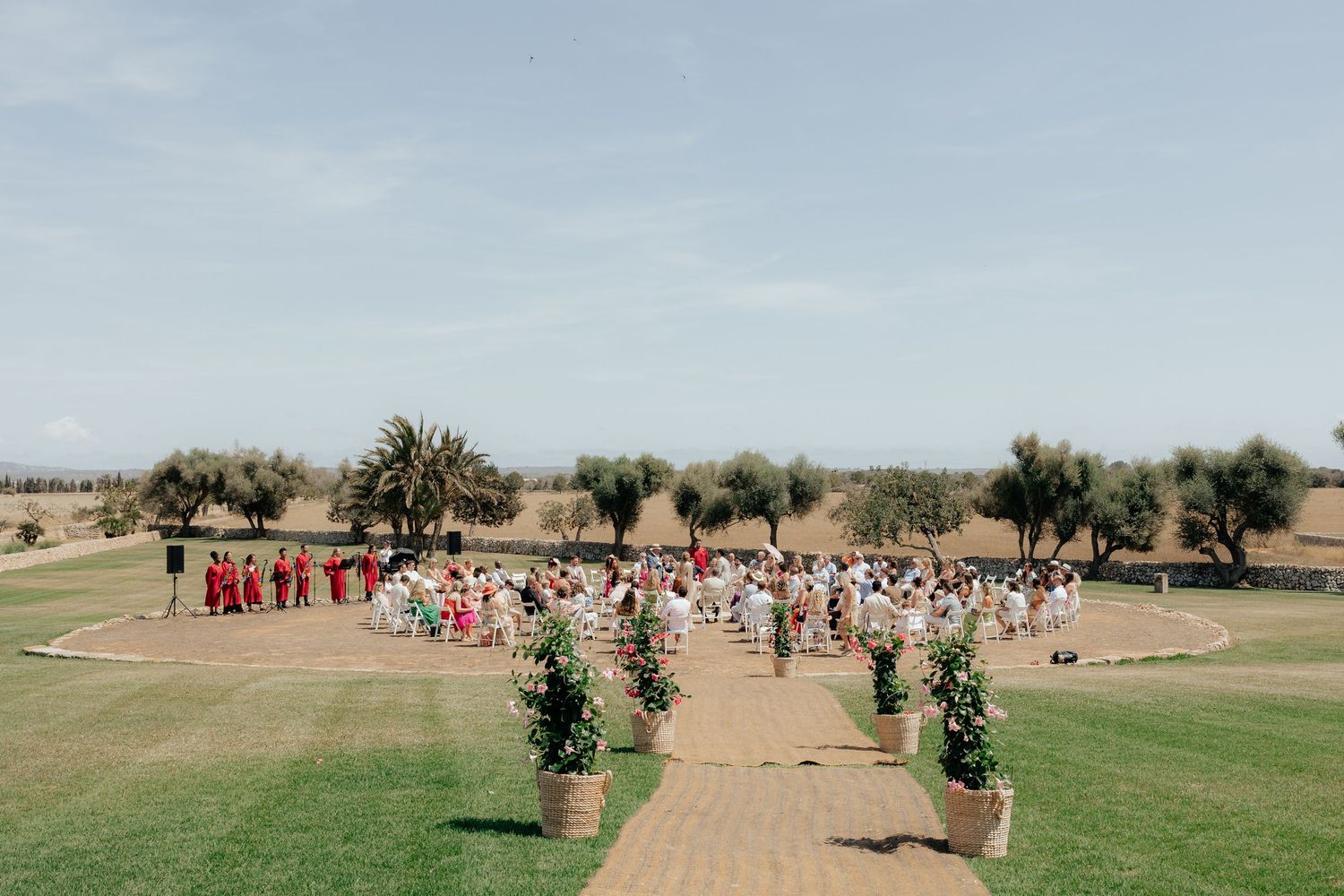 Scenic outdoor wedding ceremony setup on a golf course with palm trees and guests gathering on a sunny day.