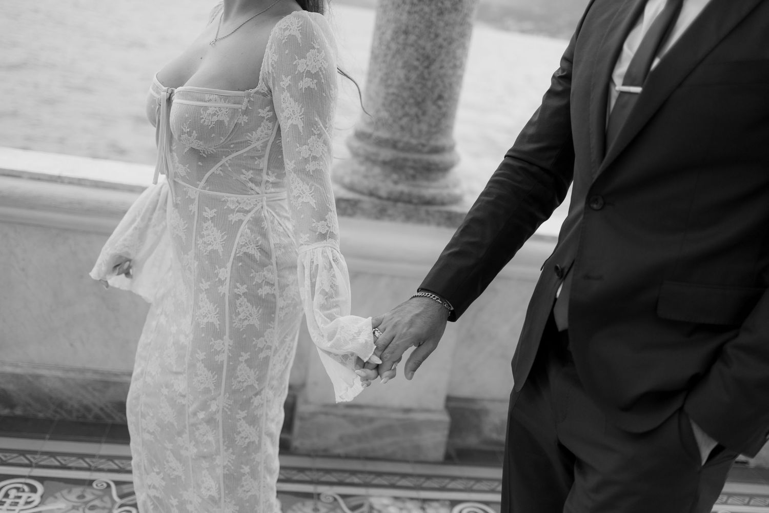 Close up black and white photo showing couple holding hands in formal wedding attire.