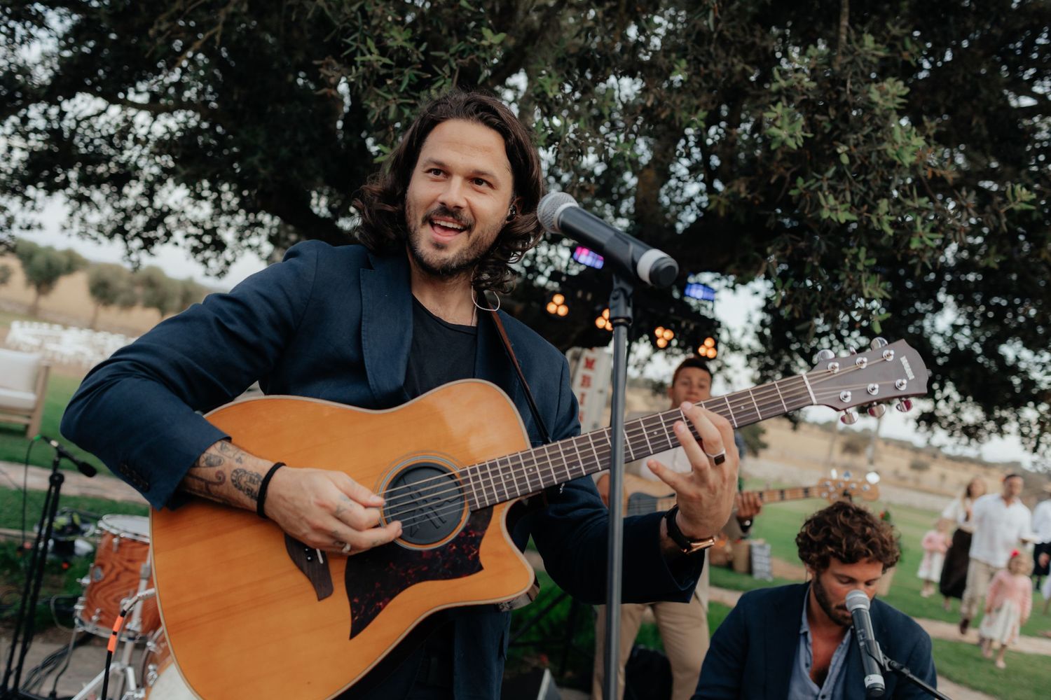 Musician playing acoustic guitar at outdoor wedding reception.