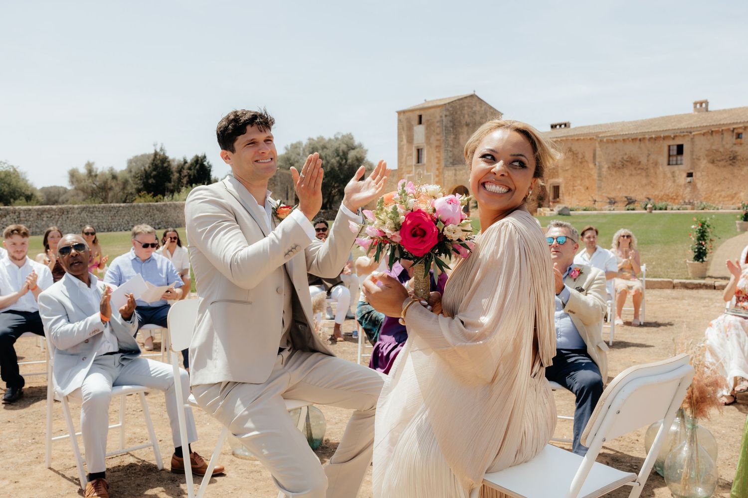 Joyful outdoor wedding celebration with guests clapping in the background.