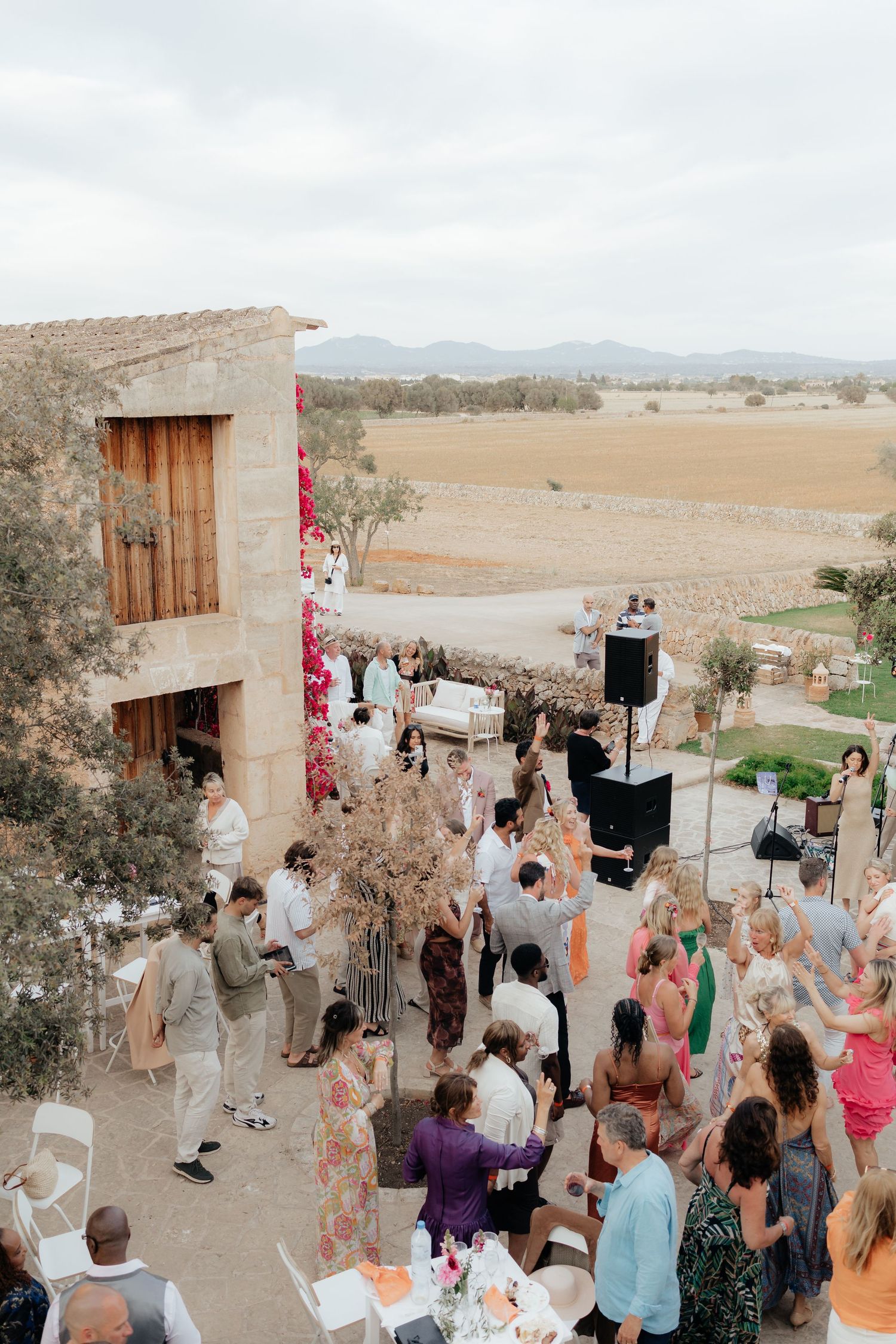 Outdoor wedding reception gathering with guests and musicians at a rustic Mediterranean venue.