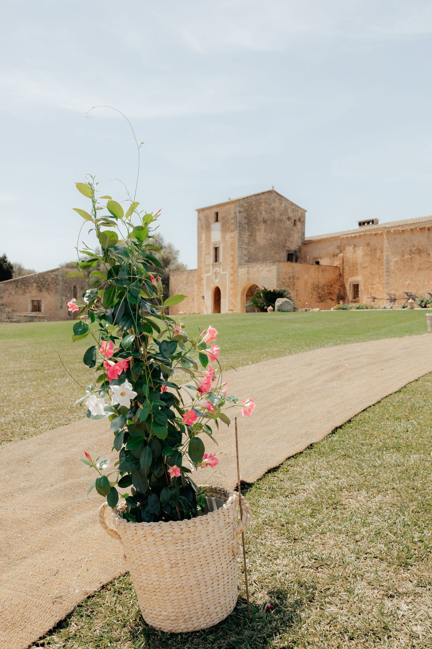 Pink flowers in a woven basket stand decoratively in front of a historic stone fortress building on a sunny day.