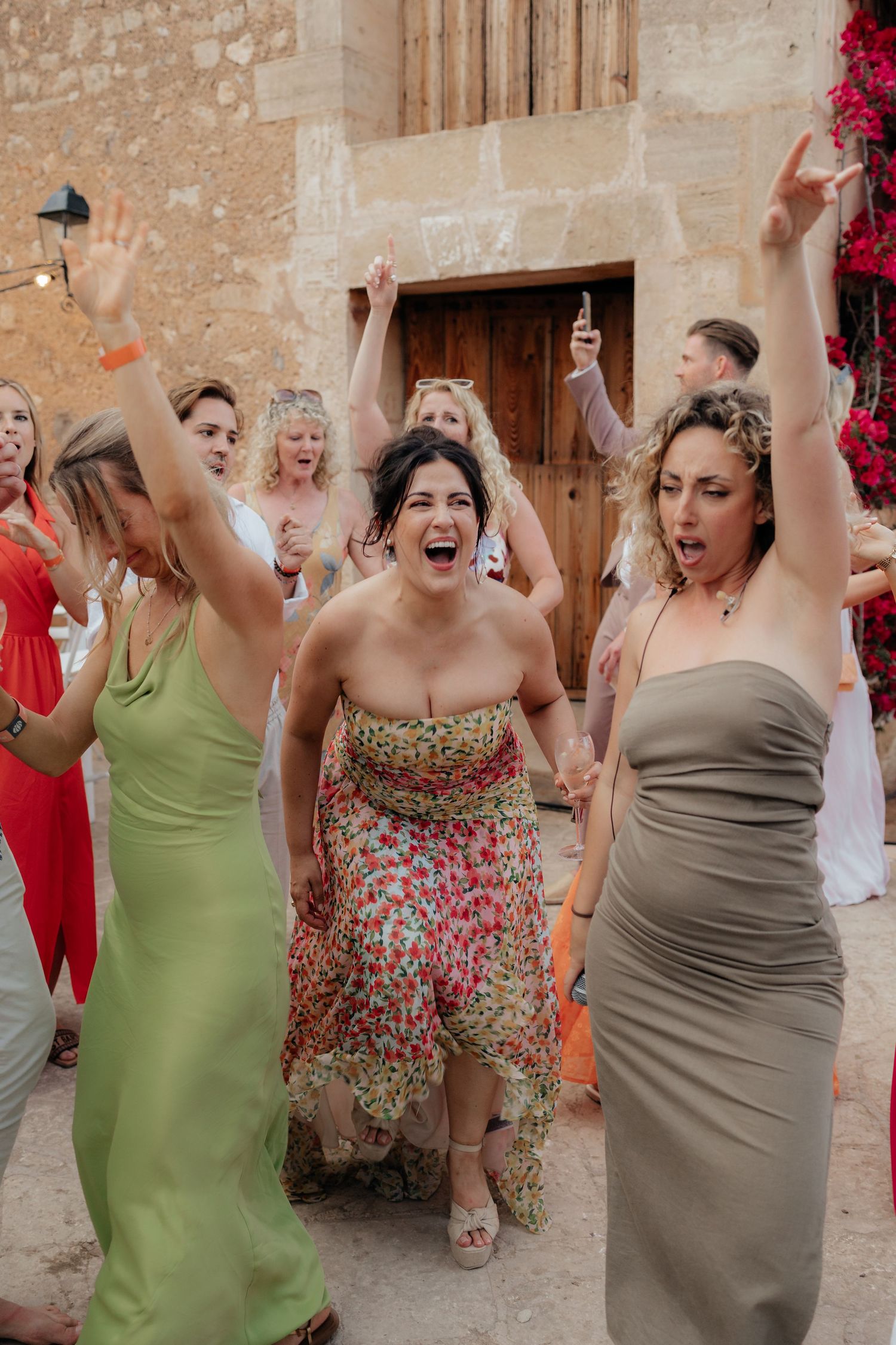 Wedding guests dancing and celebrating joyfully outside a historic stone building.