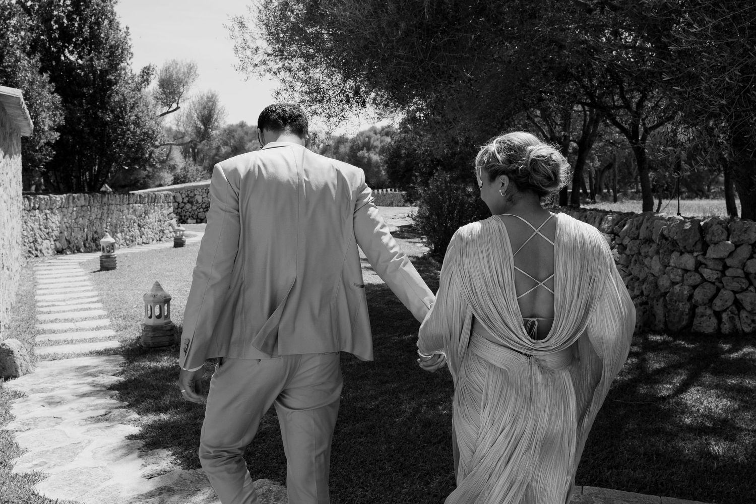 Couple walking down garden path in flowy wedding attire.