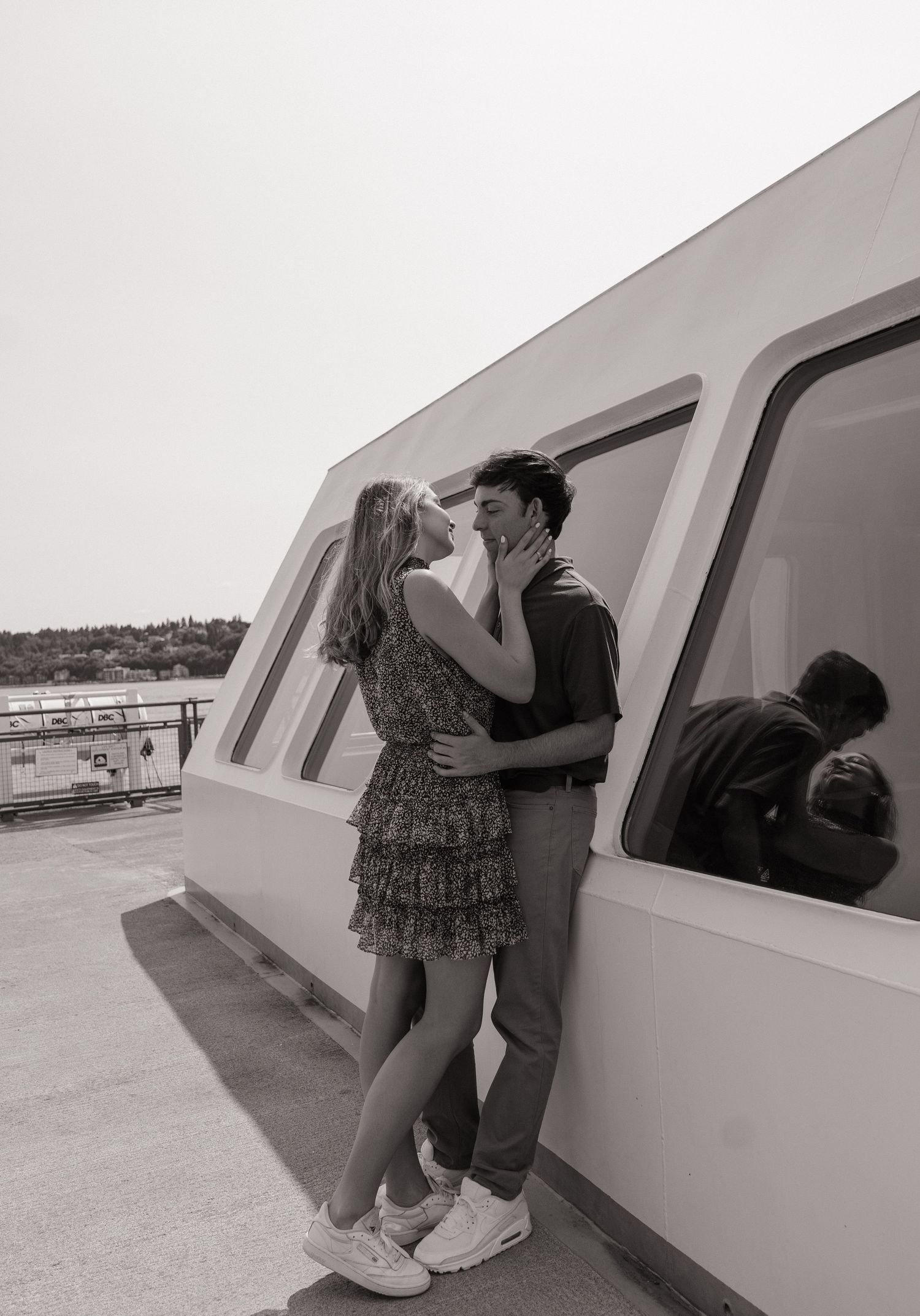 Black and white photo of a couple sharing an intimate near-kiss against a ferry cabin wall, their reflection visible in the window.