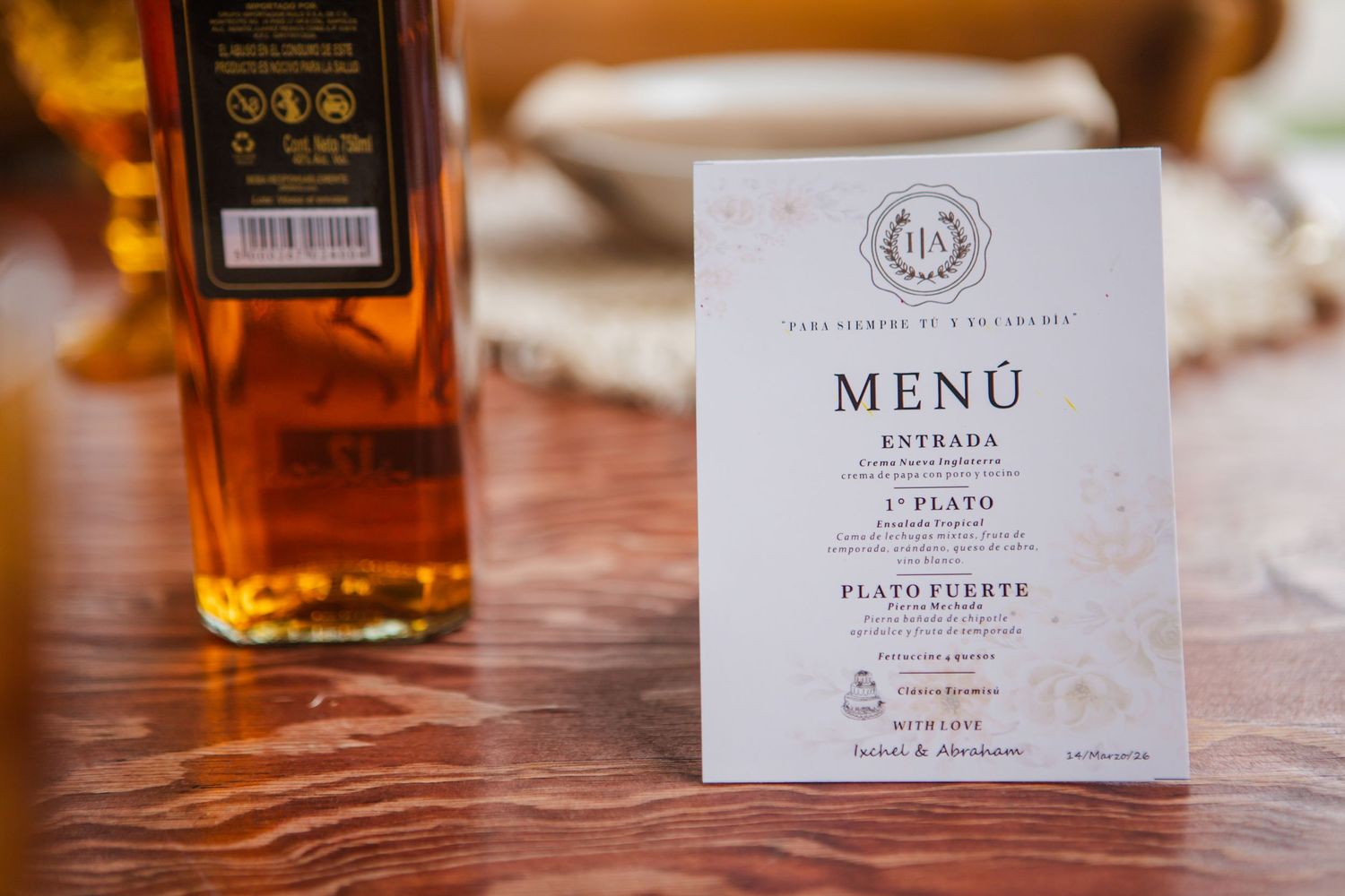Elegant printed wedding menu card with Spanish courses beside an amber liquor bottle on a rustic polished wooden table.