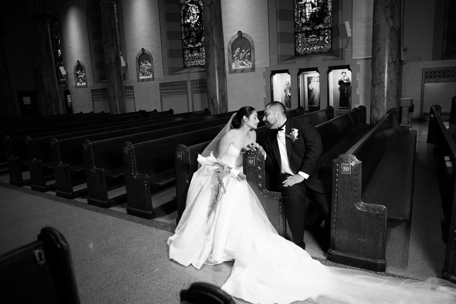 Bride and groom share an intimate moment between wooden pews in a church in this black and white wedding photo.