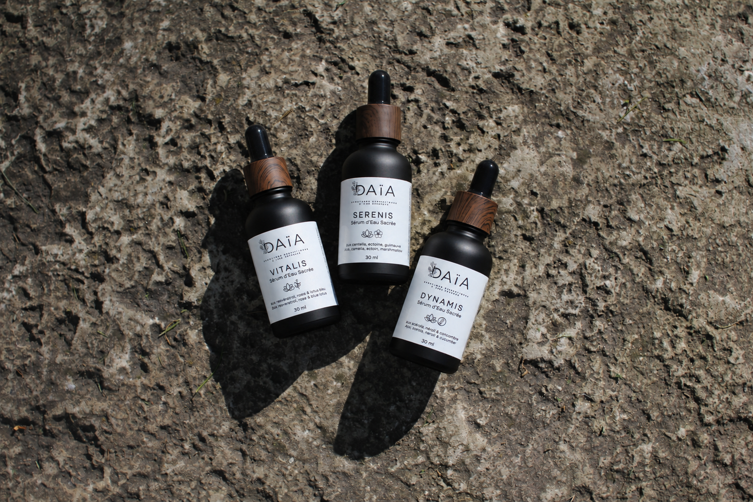 Three DAIA brand dropper serum bottles arranged on a textured stone surface in natural light.