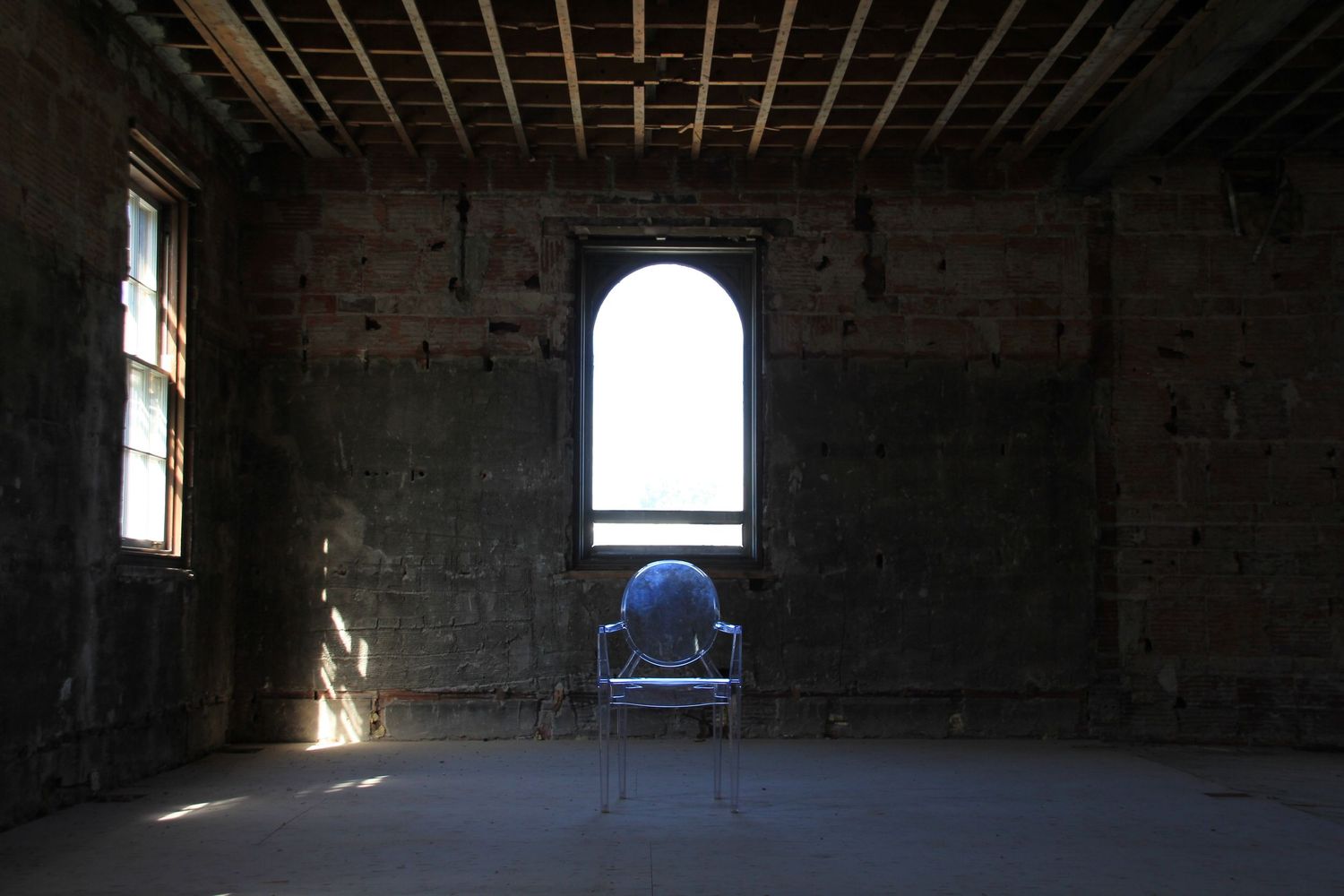 Ornate chair placed in an empty abandoned brick room with an arched window and natural light.