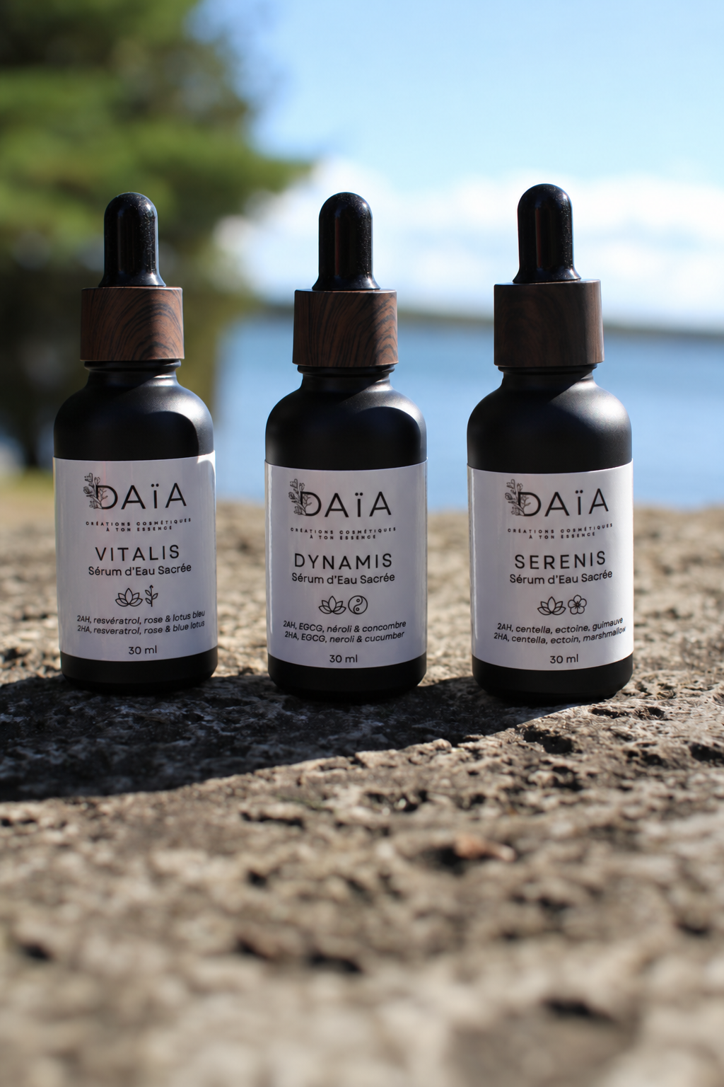 DAIA skincare trio featuring Vitalis, Dynamis, and Serenis serums on a rocky outdoor surface.