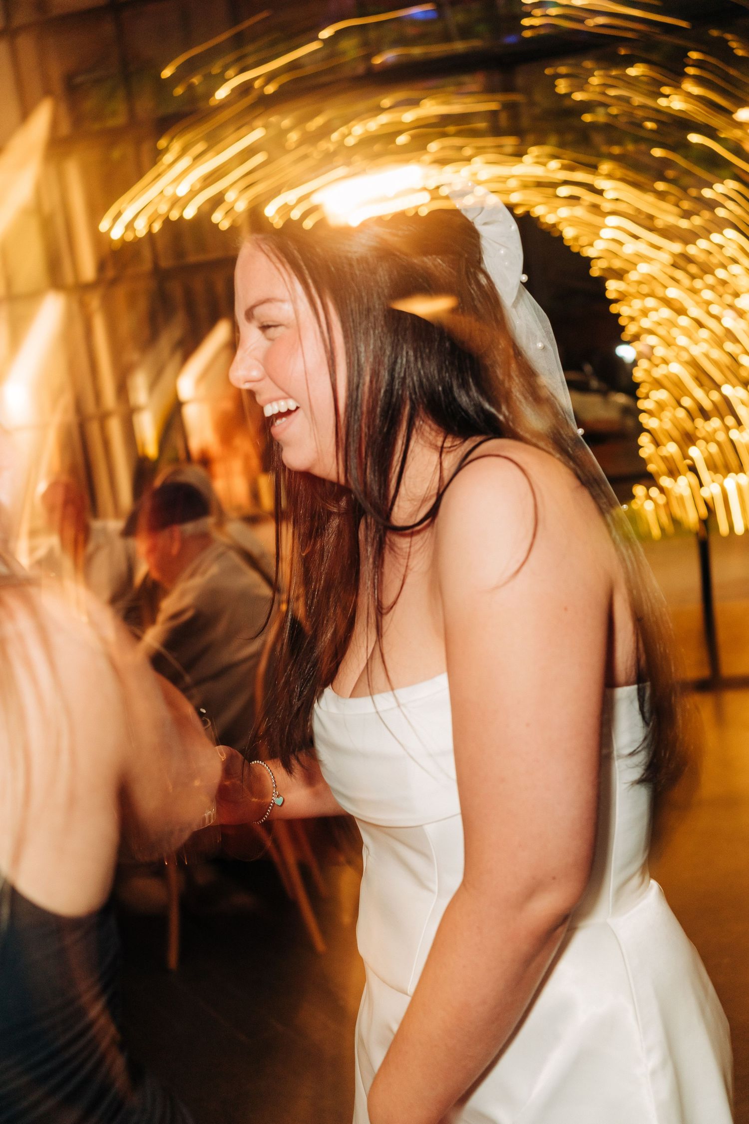 Bride with friends under warm lights at a post wedding party