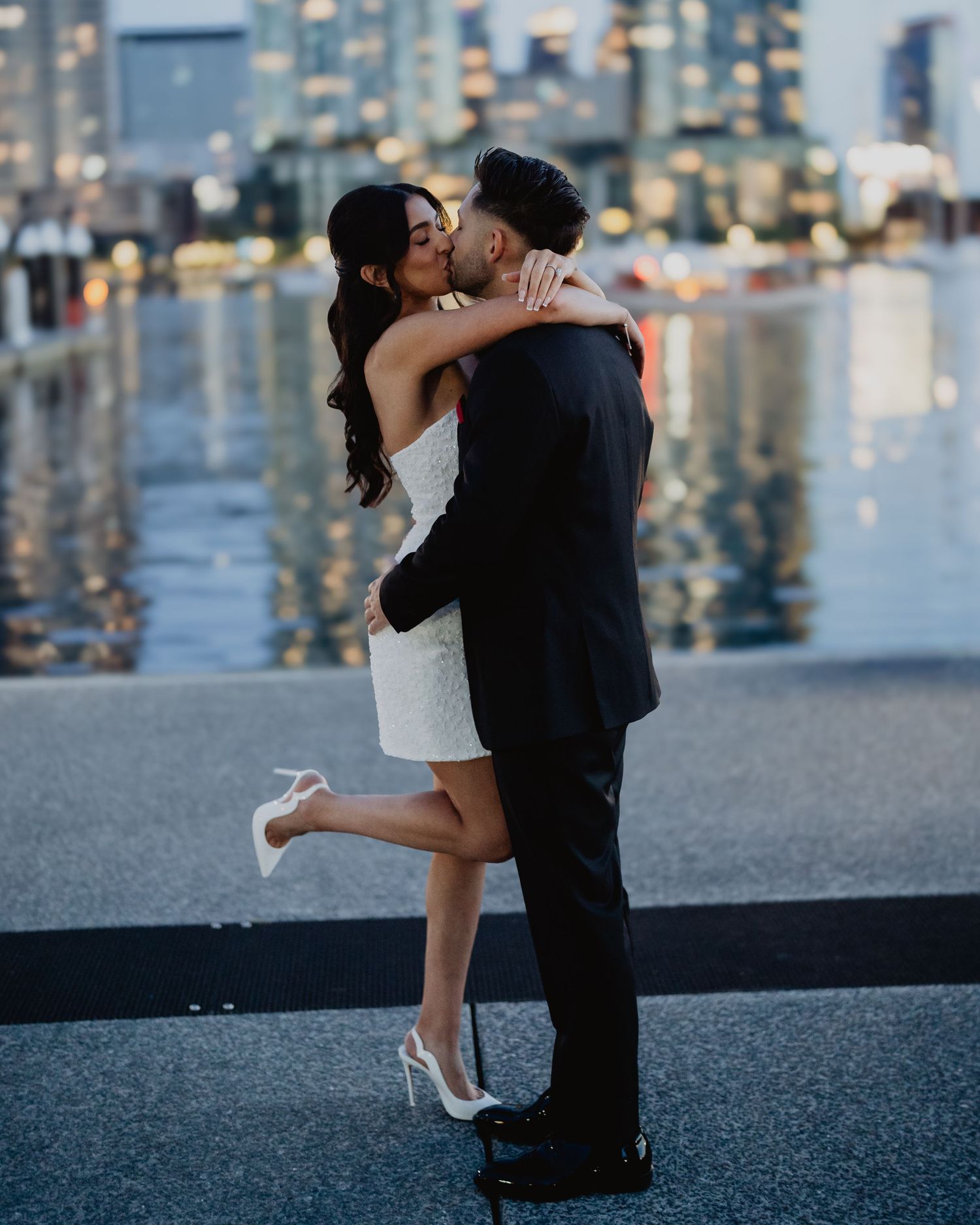Couple embracing by the water at night with Melbourne city lights behind them