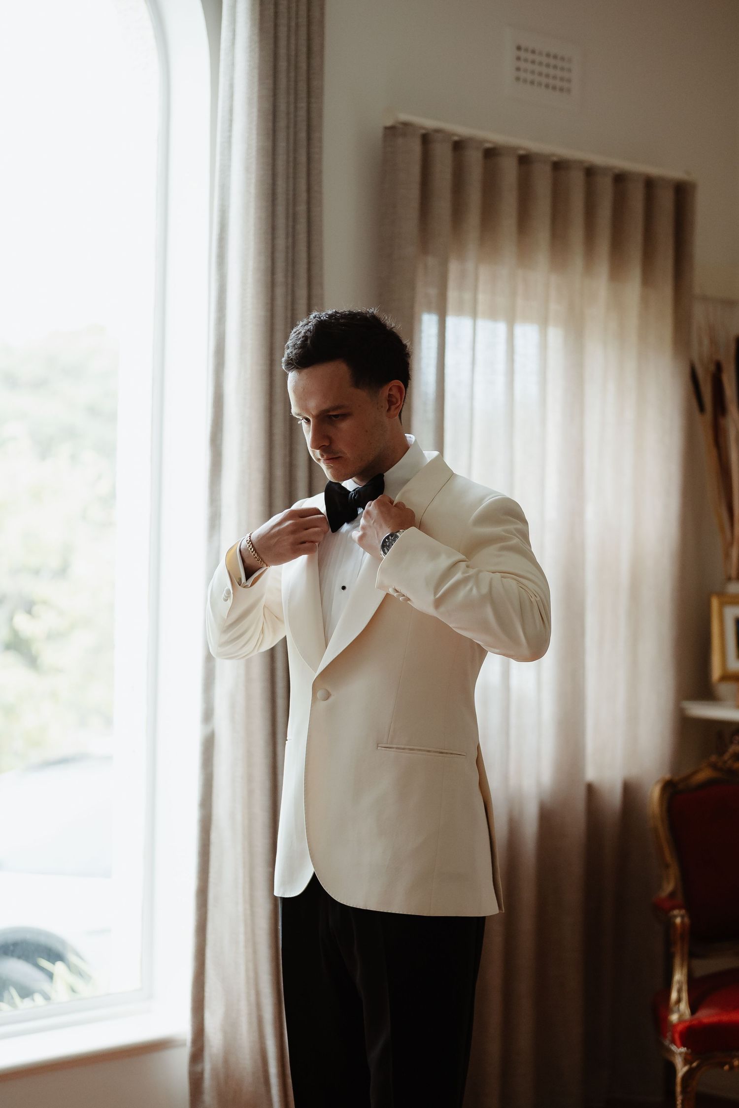 Groom adjusting his bow tie by the window before a Melbourne wedding