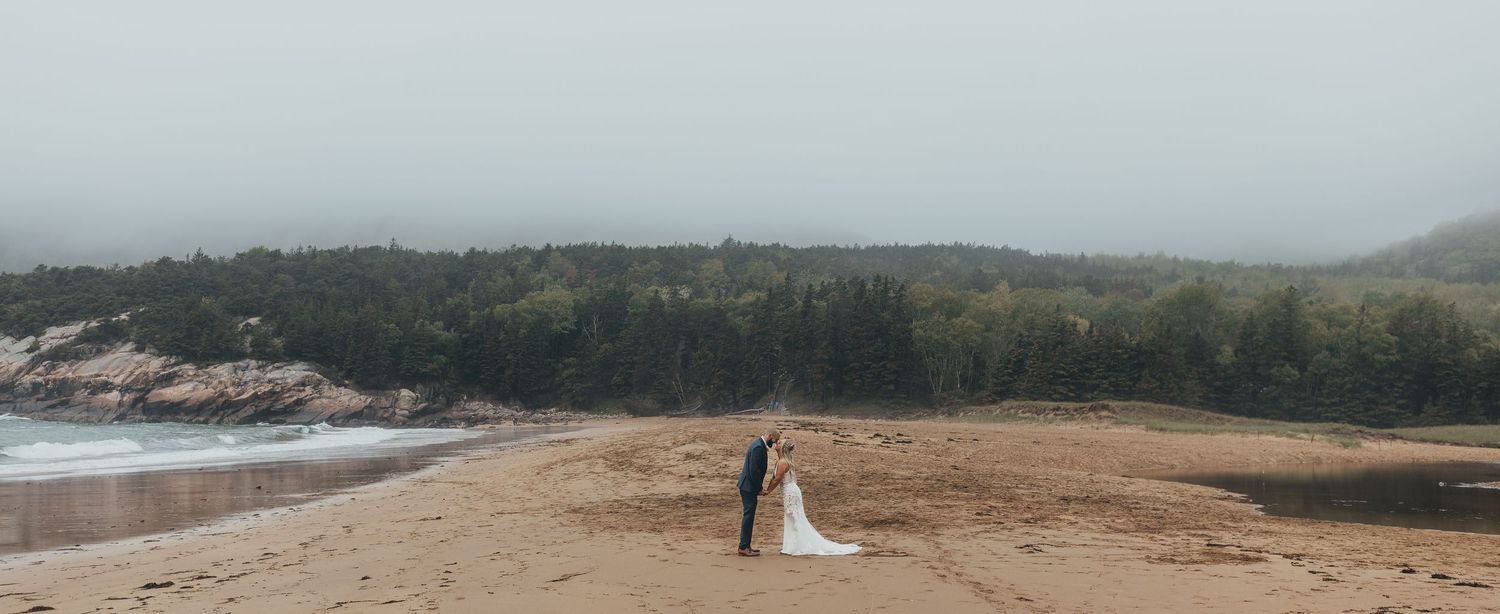 Romantic wedding photos captured on a misty beach with rocky cliffs and ocean waves in the background Acadia National Park, Bar Harbor Maine
