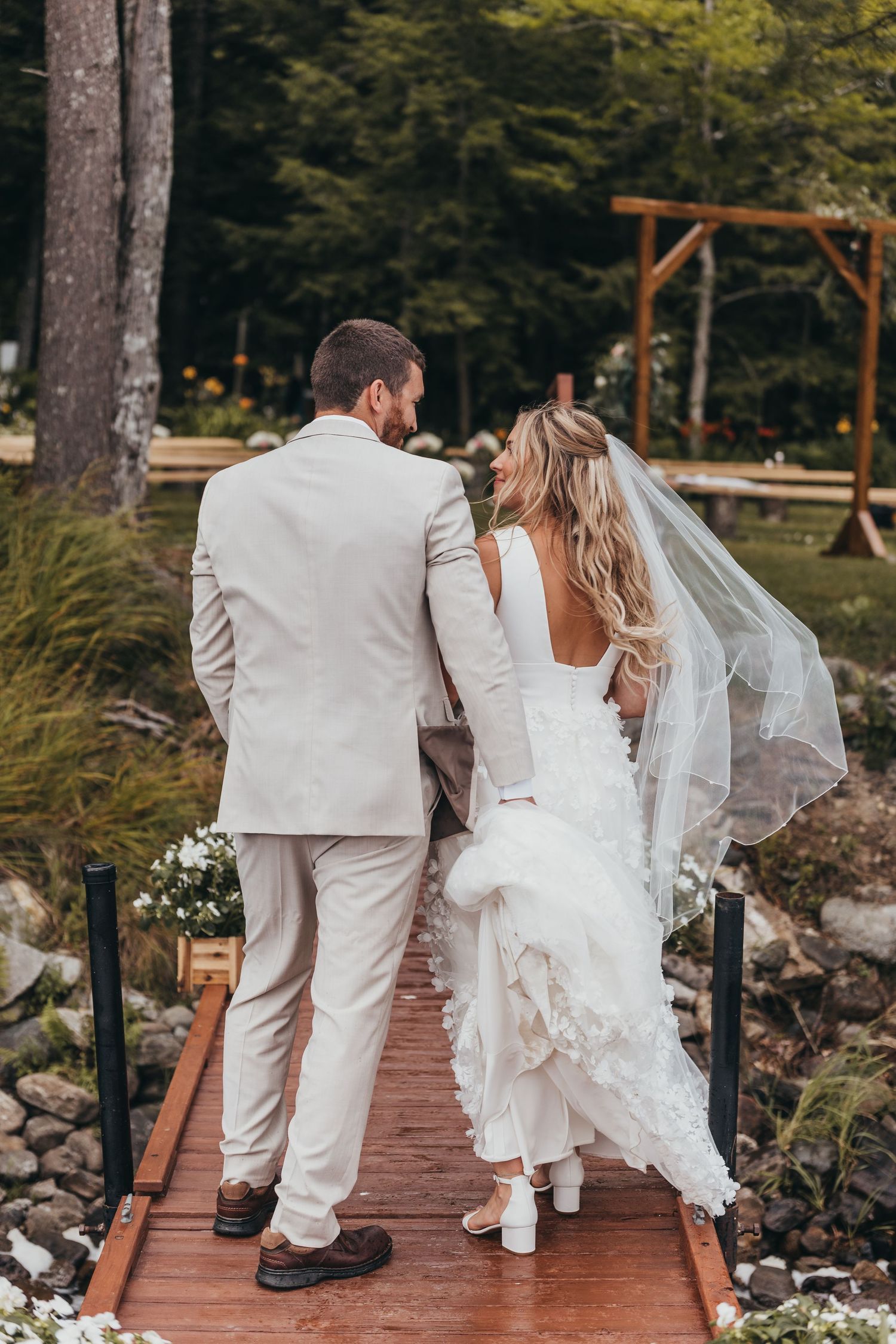 Wedding couple walking on a wooden bridge surrounded by lush forest scenery.
