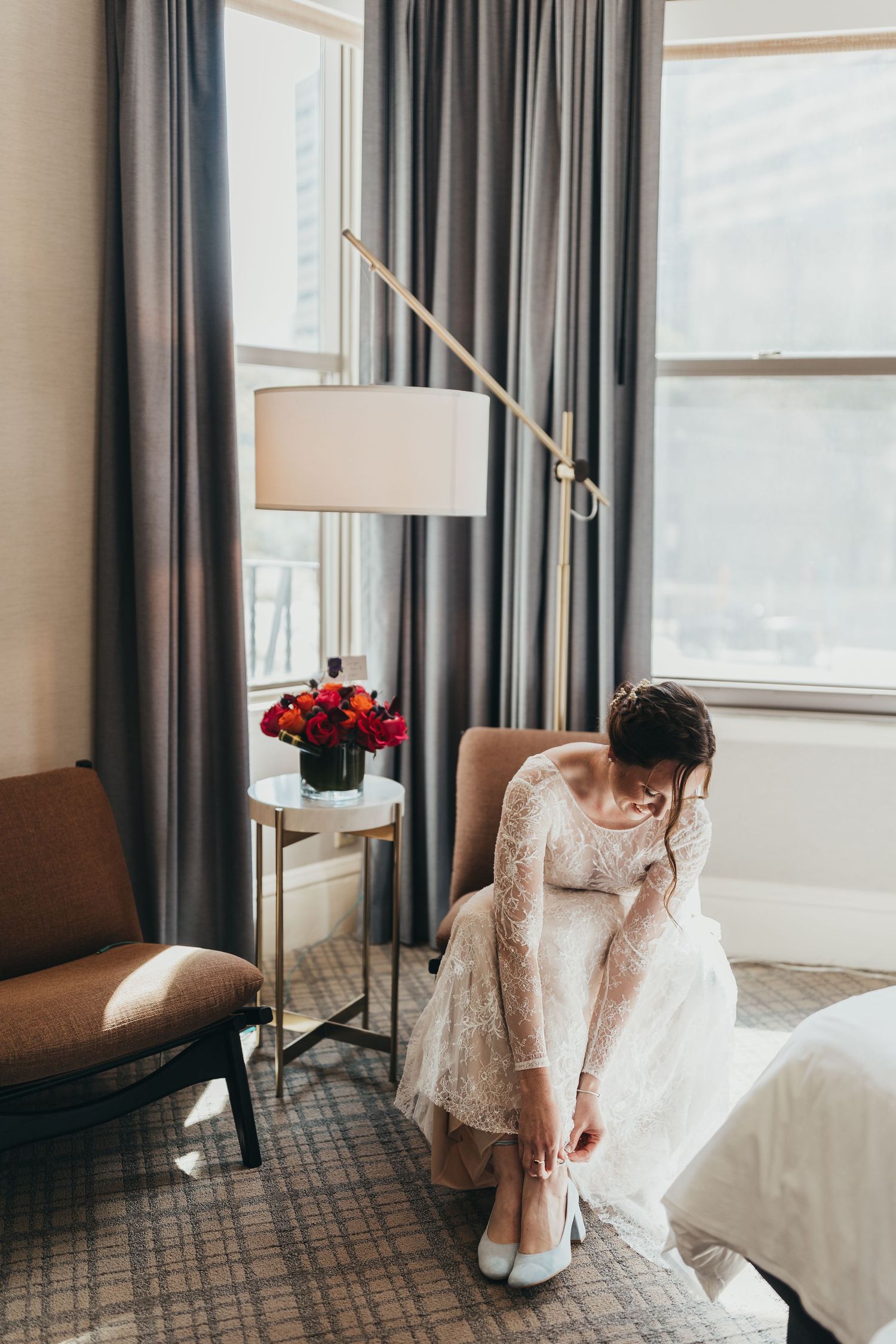 Close-up of wedding dress details in a hotel room with grey curtains.