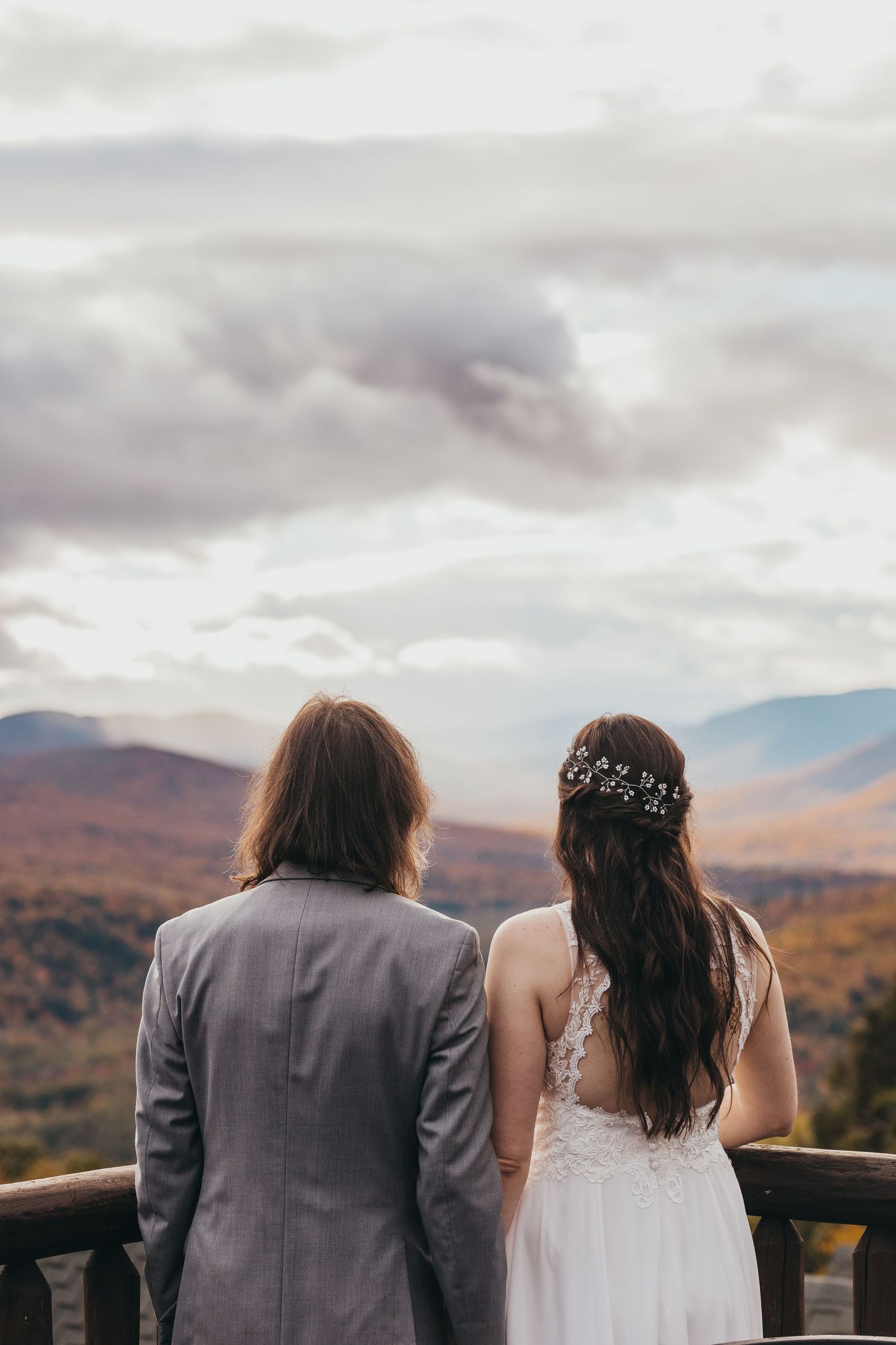 Couple overlooking mountain vista on their wedding day with cloudy skies.
