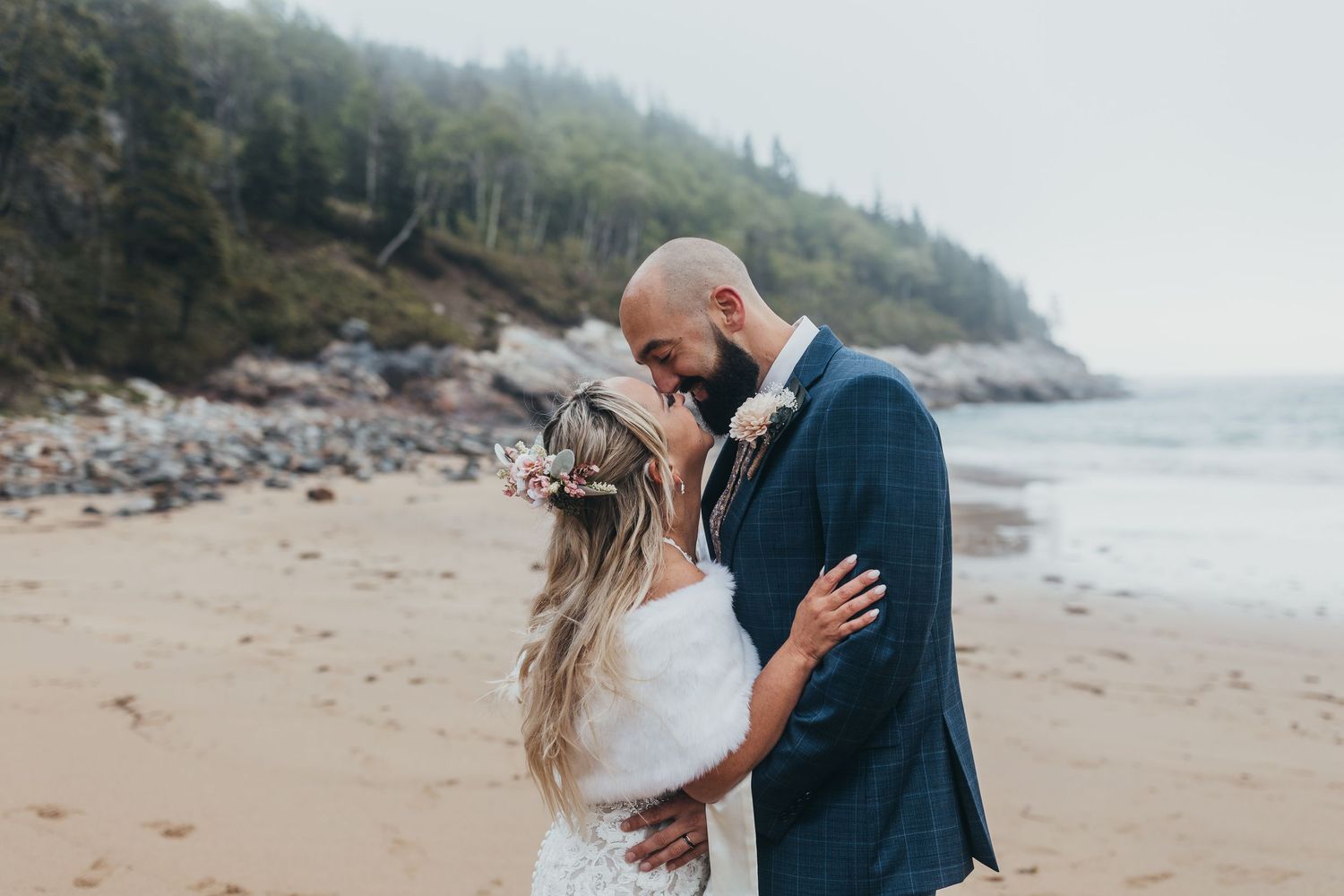 Couple embracing on a scenic coastal beach with dramatic cliffs and fog in the distance. Acadia National Park, Bar Harbor Maine