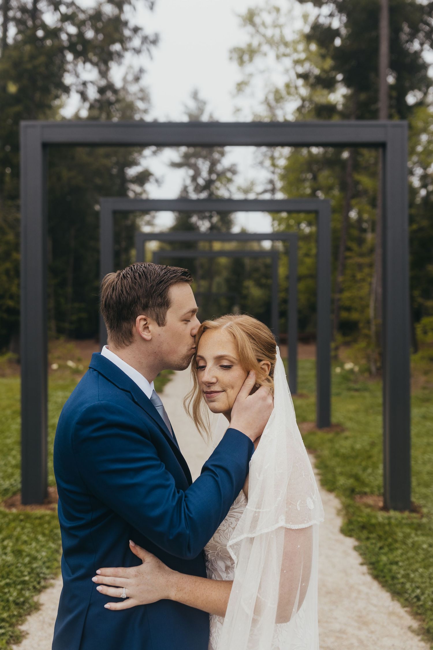 Wedding couple sharing intimate moment in garden pathway lined with metal archways.